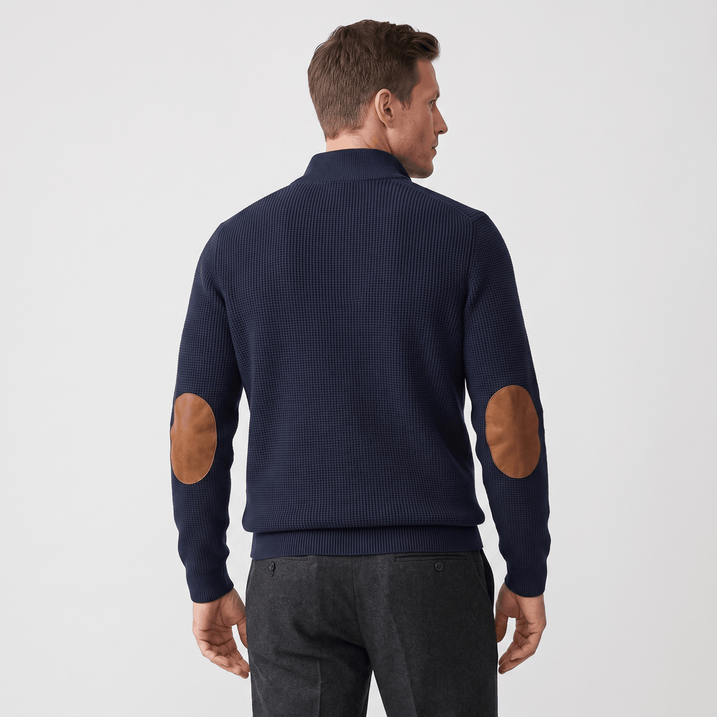 Navy blue ribbed knit sweater featuring a stand collar and contrasting brown elbow patches, worn with dark trousers.