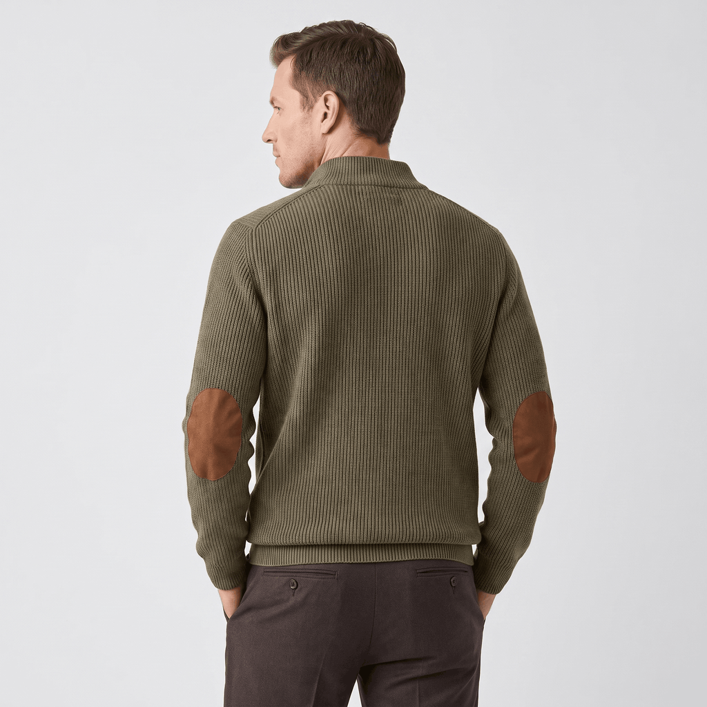 Olive green ribbed knit henley sweater with brown contrast elbow patches and a stand collar, worn over dark trousers.