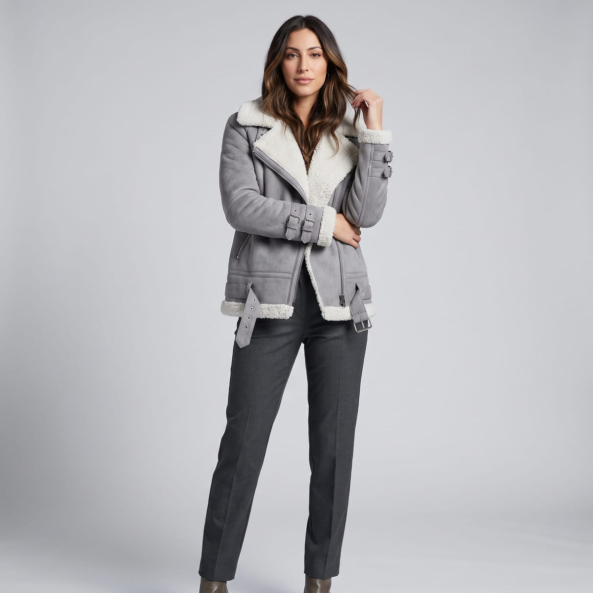 A woman wearing a gray leather shearling aviator jacket with an asymmetric zip and buckled strap, adjusting the collar