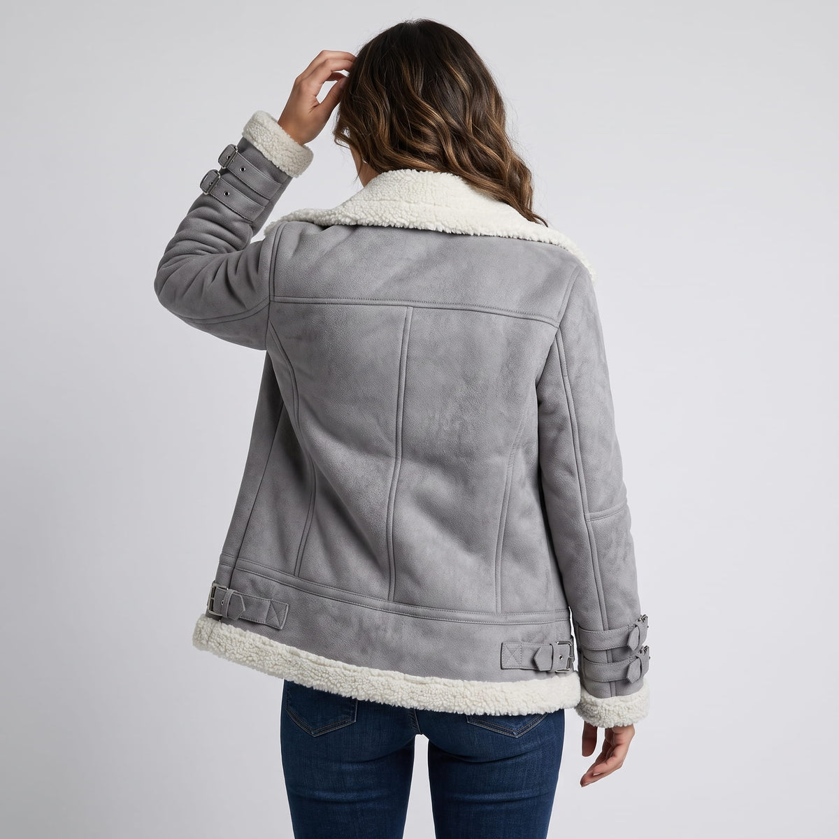 A woman wearing a gray leather shearling aviator jacket with an asymmetric zip and buckled strap, shown from the back