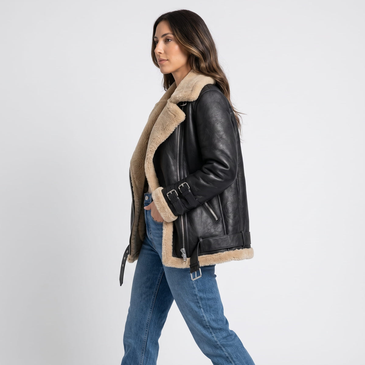 A woman wearing a black leather shearling aviator jacket with an asymmetric zip and buckled strap, shown in side view