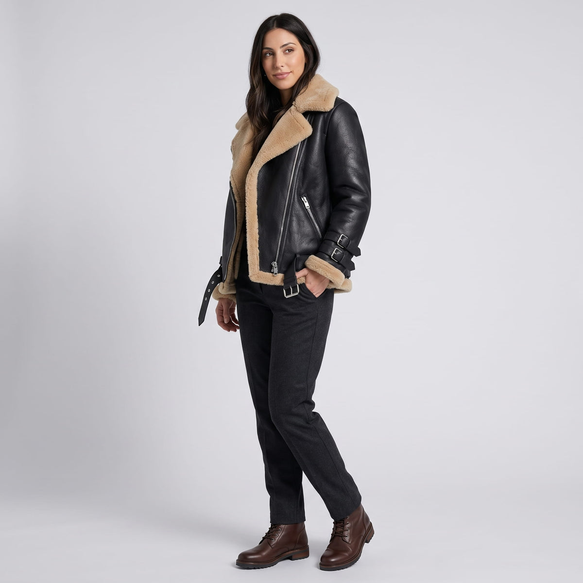 A woman wearing a black leather shearling aviator jacket with an asymmetric zip and buckled strap, standing indoors
