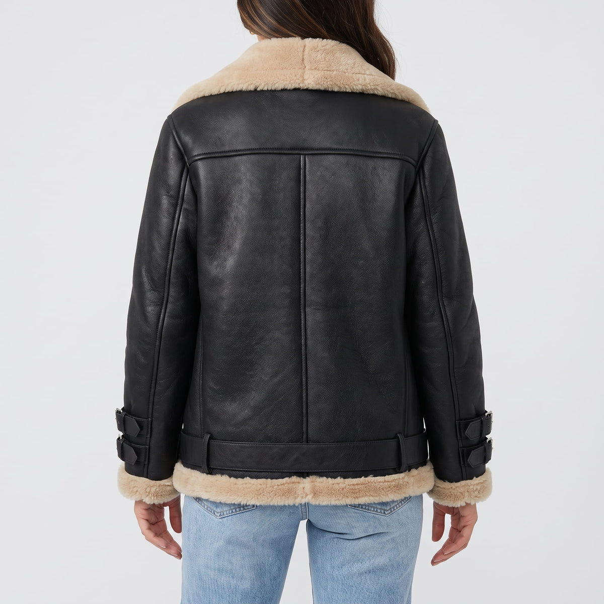 A woman wearing a black leather shearling aviator jacket with an asymmetric zip and buckled strap, shown from the back