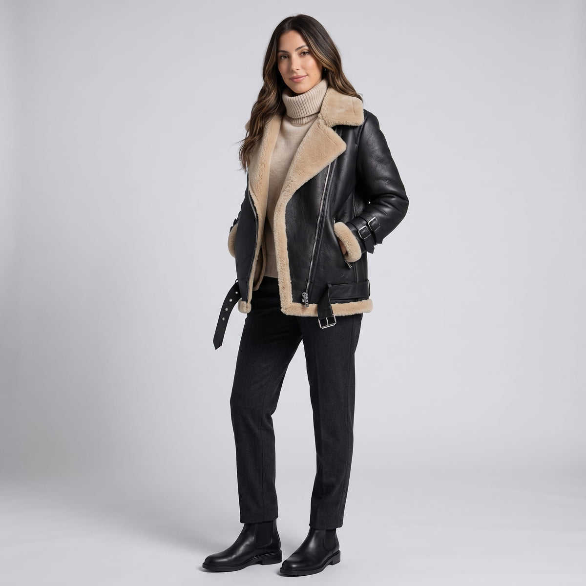 A woman wearing a black leather shearling aviator jacket with an asymmetric zip and buckled strap, full-length view