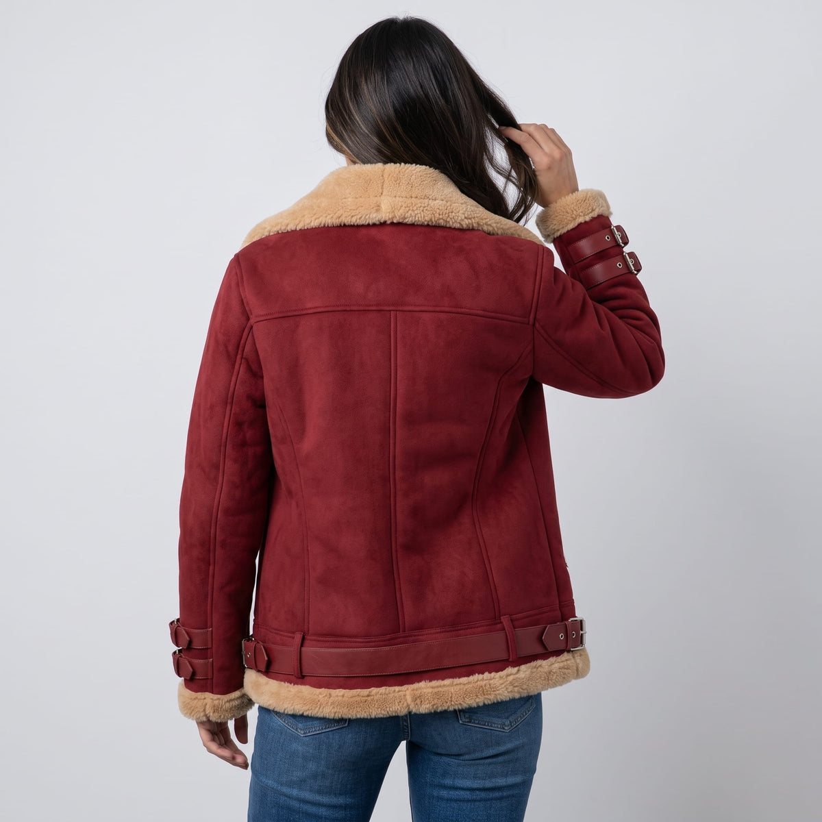 A woman wearing a burgundy leather shearling aviator jacket with an asymmetric zip and buckled strap, shown from the back