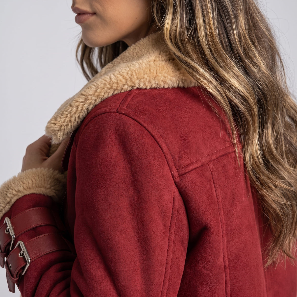 A woman wearing a burgundy leather shearling aviator jacket with an asymmetric zip and buckled strap, shown from the back