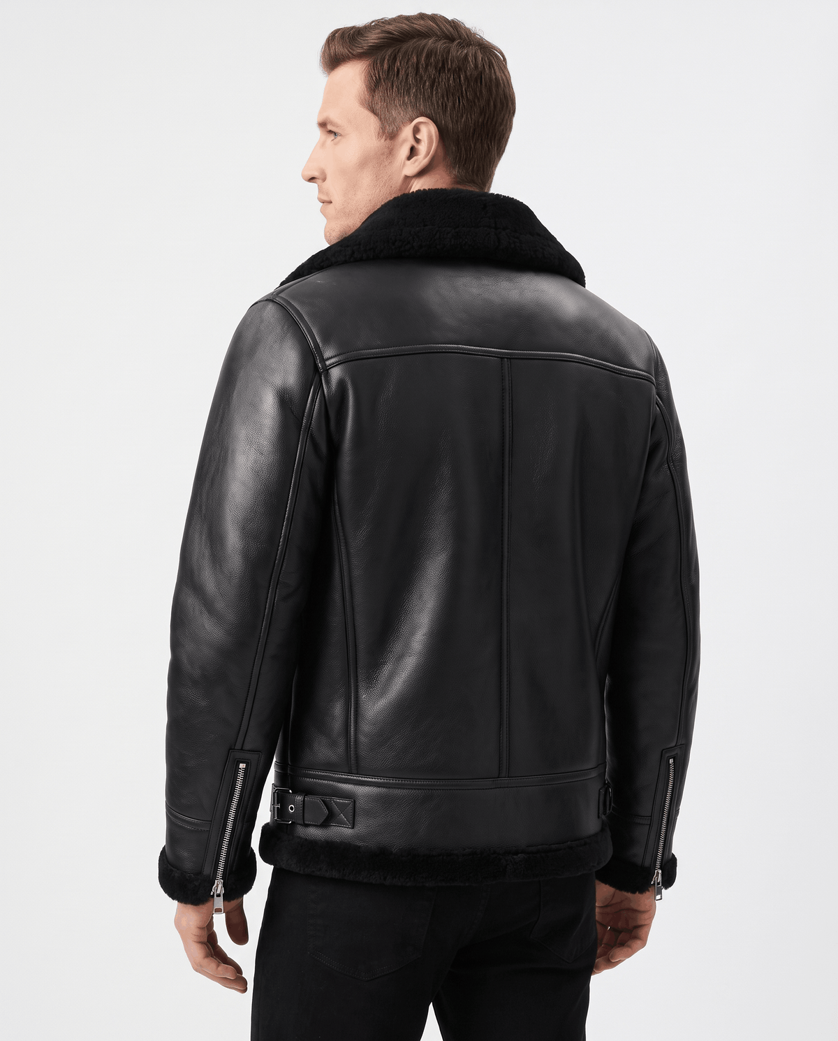 A man wearing a black leather shearling aviator jacket with an asymmetrical zip and buckle strap, shown from the back