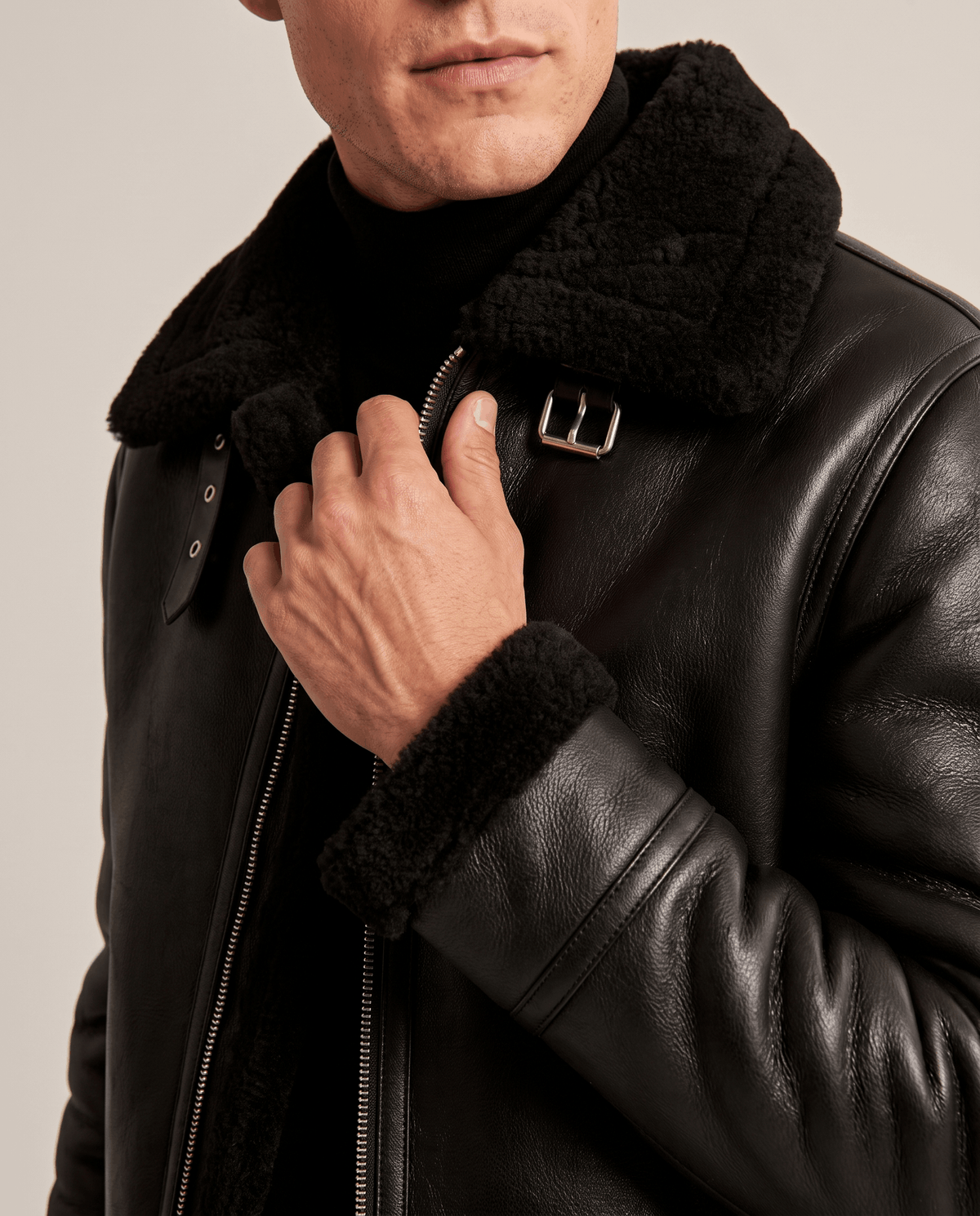 Close-up of a man wearing a black leather shearling aviator jacket, showing the plush collar and front closure