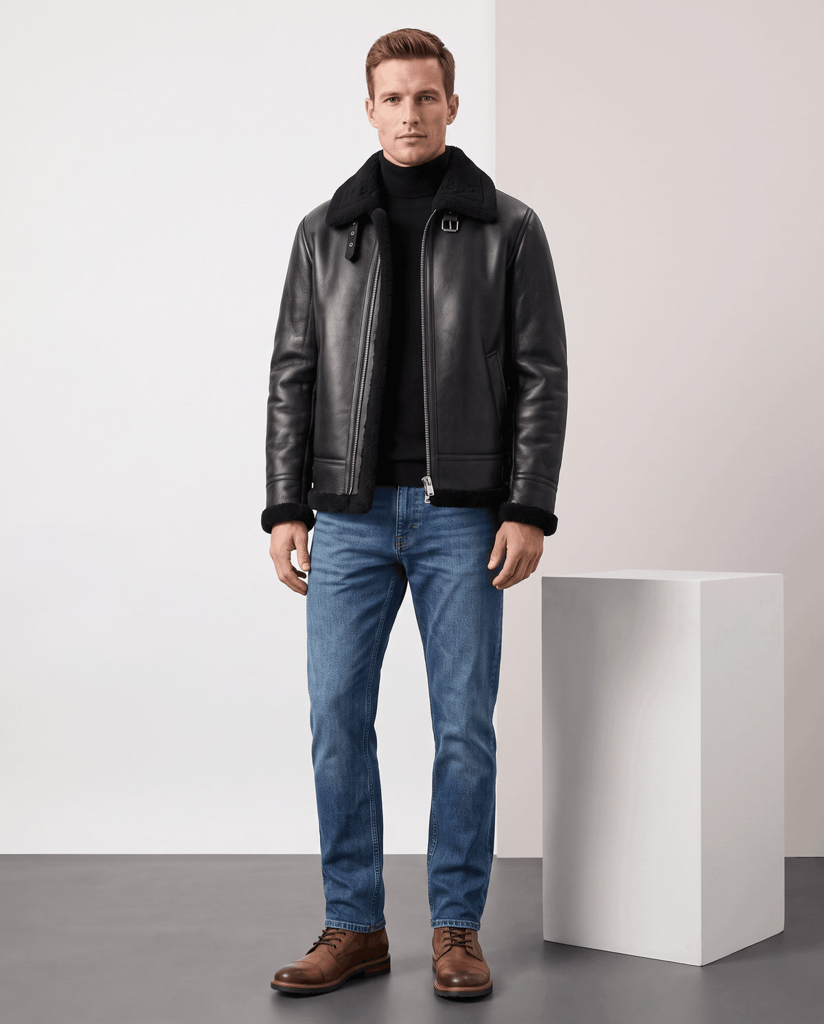 A man wearing a black leather shearling aviator jacket with an asymmetrical zip and buckle strap, full-length view