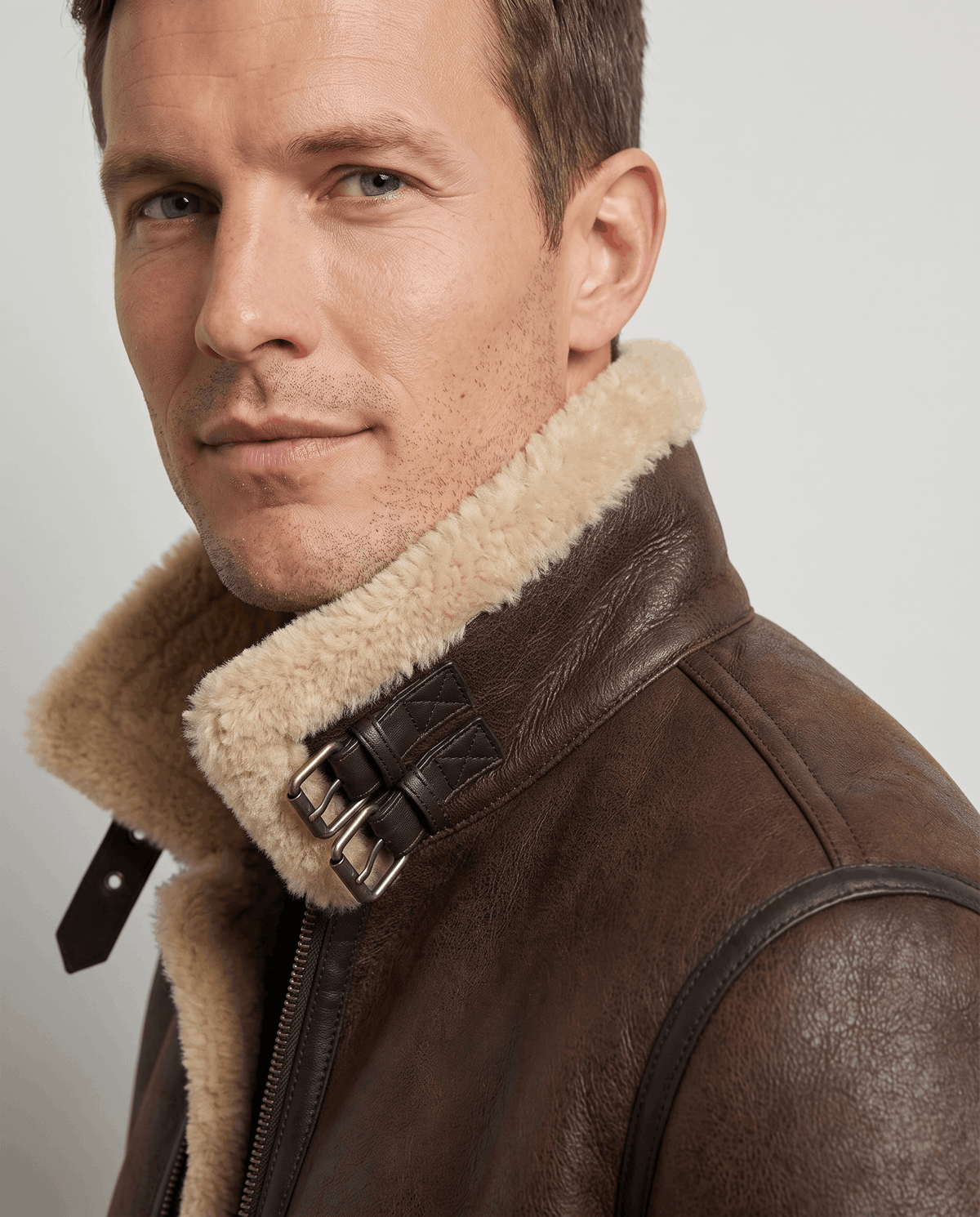 Close-up of a brown leather shearling aviator jacket showing the shearling collar and buckle strap detail