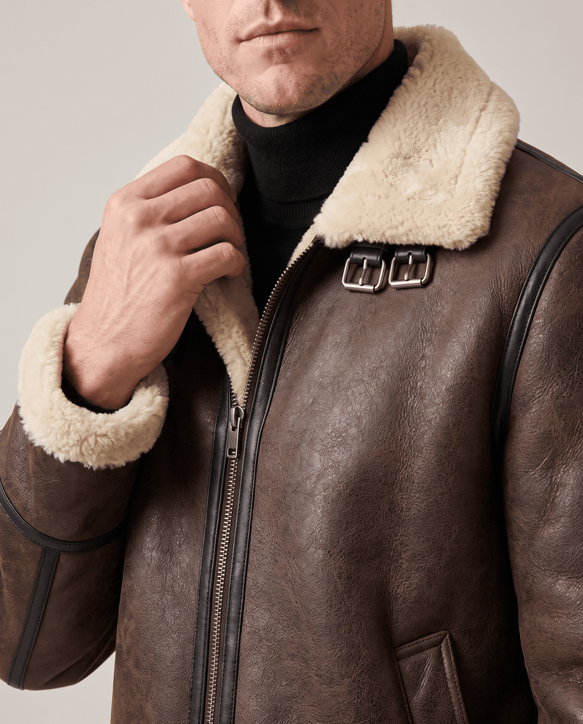 Close-up of a man wearing a brown leather shearling aviator jacket with a shearling collar and buckle strap