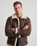 A man wearing a brown leather shearling aviator jacket with an asymmetrical zip and buckle strap