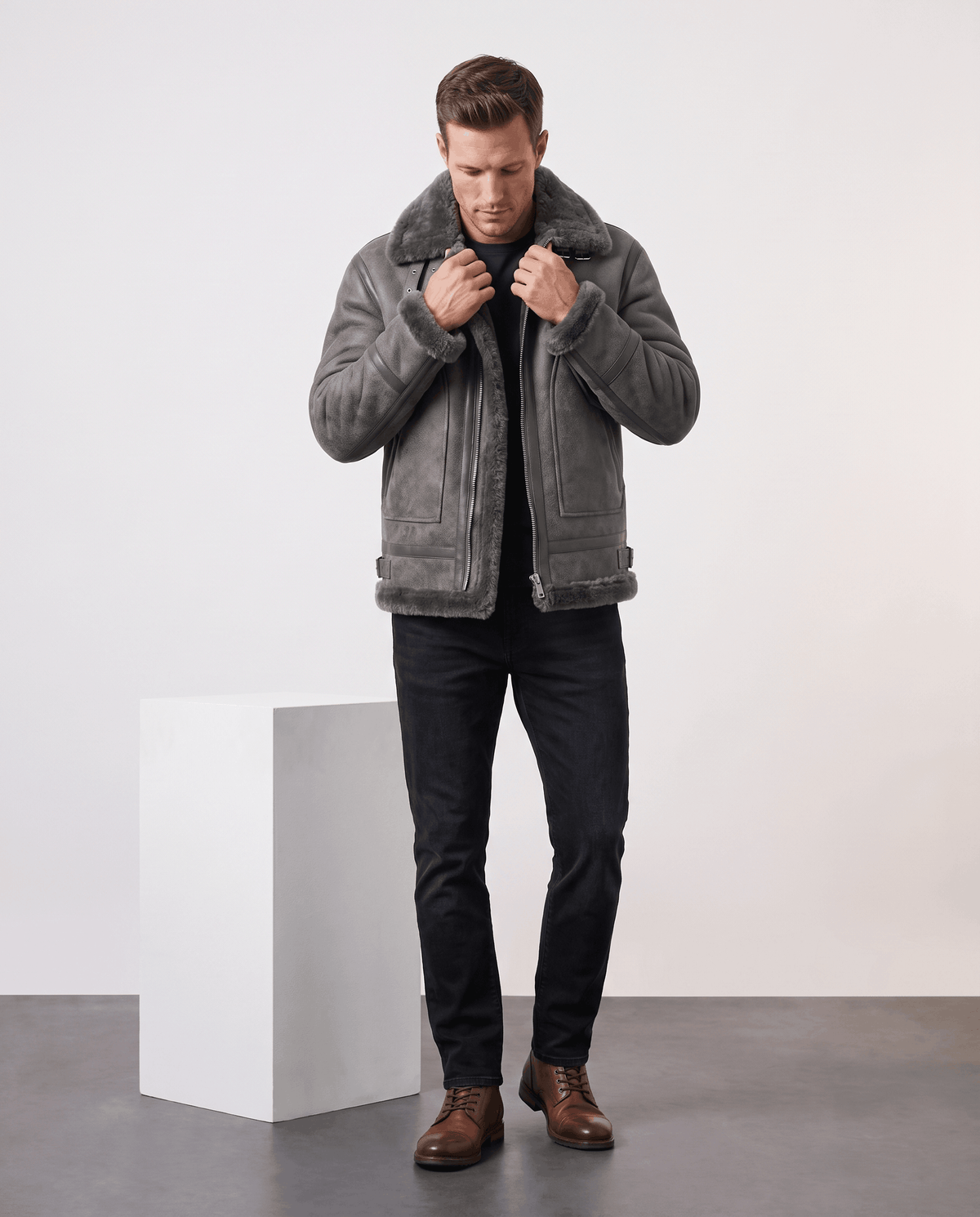 A man wearing a gray leather shearling aviator jacket with a distressed finish and lamb fur lining, standing indoors