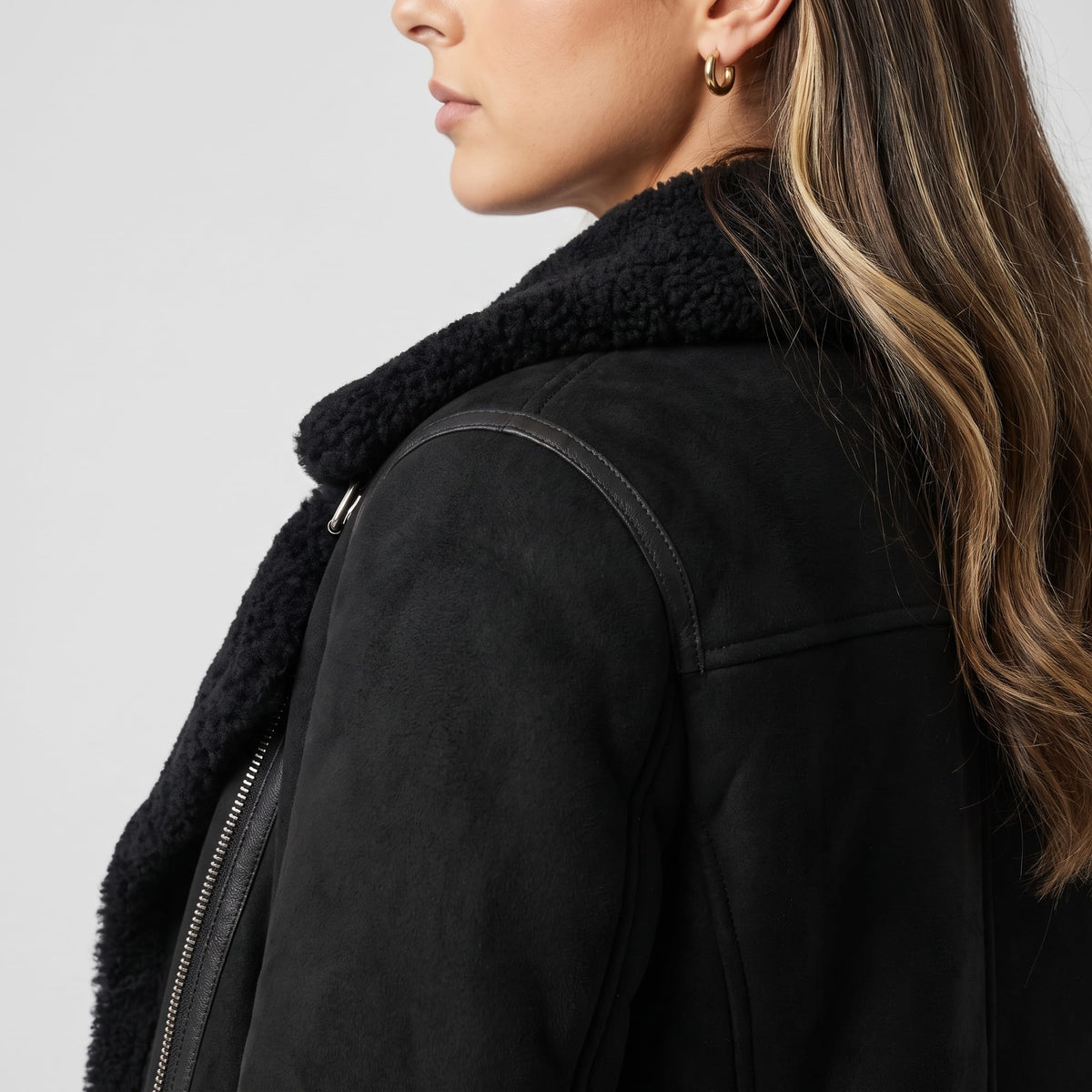 Close-up of a woman wearing a black leather shearling aviator jacket, showing the oversized shearling collar