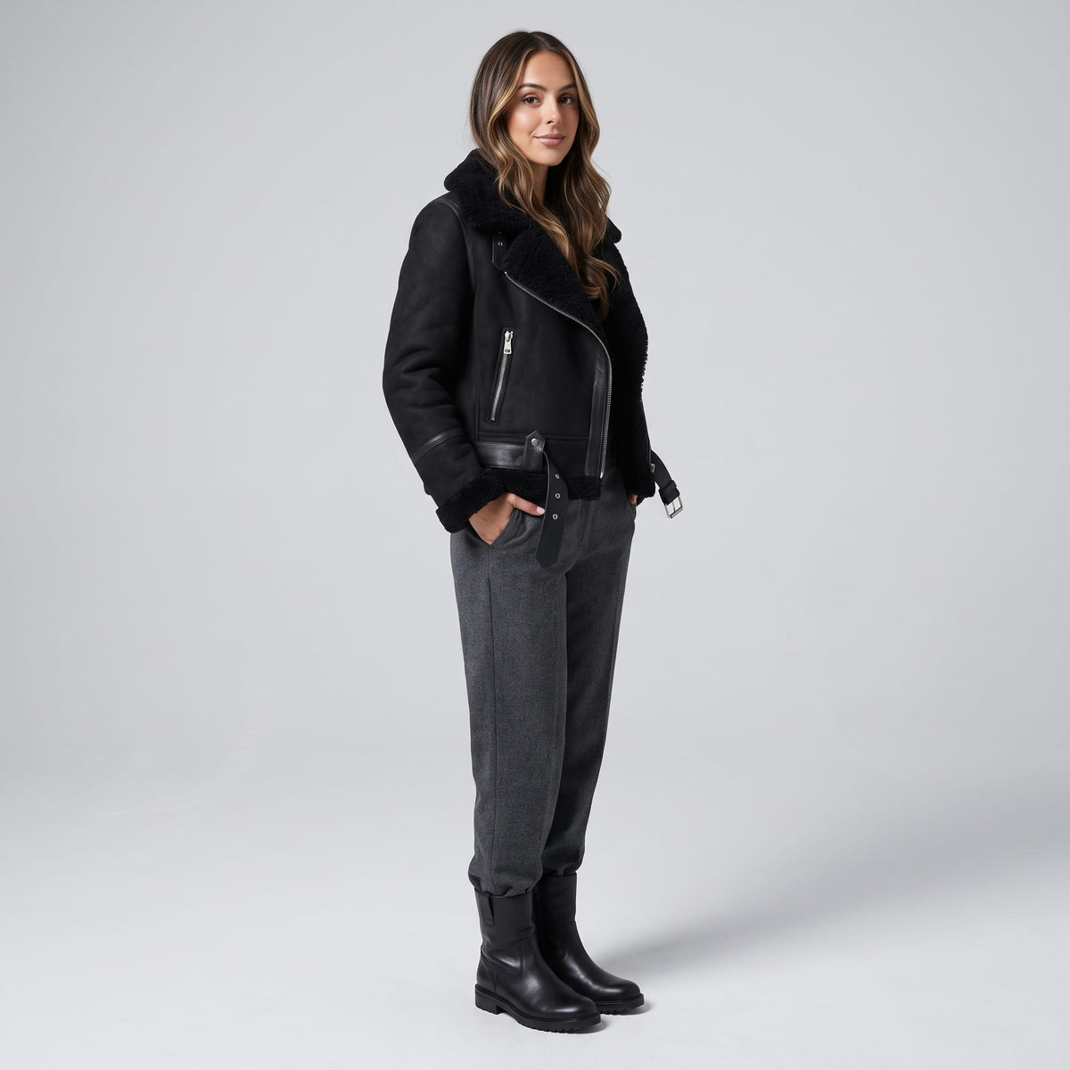 A woman wearing a black leather shearling aviator jacket with an oversized collar and belted waist, shown in side view