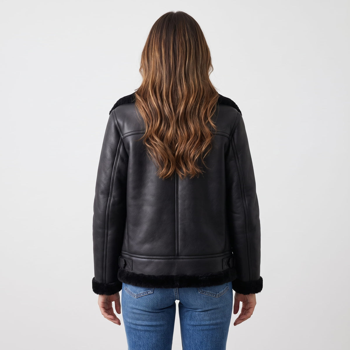 A woman wearing a black leather shearling biker jacket with plush trim, shown from the back