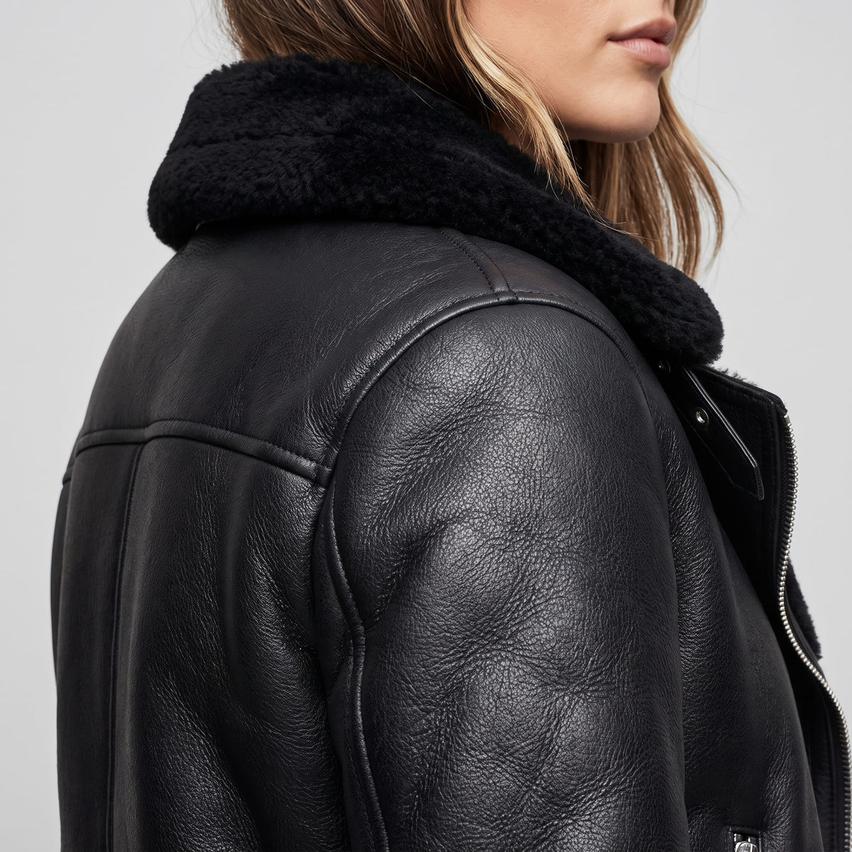 Close-up of a black leather shearling biker jacket showing the plush trim and asymmetrical zip