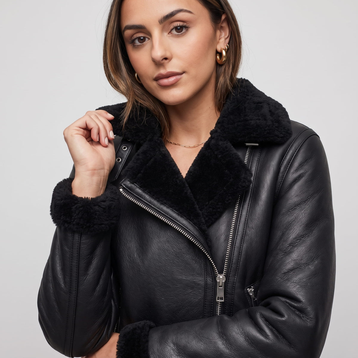 Close-up of a woman wearing a black leather shearling biker jacket, showing the plush collar and zip front