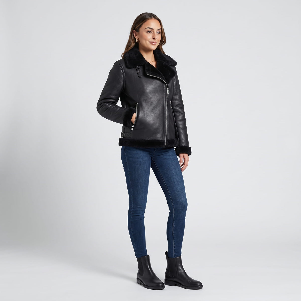 A woman wearing a black leather shearling biker jacket with an asymmetrical zip and plush trim, shown in side view