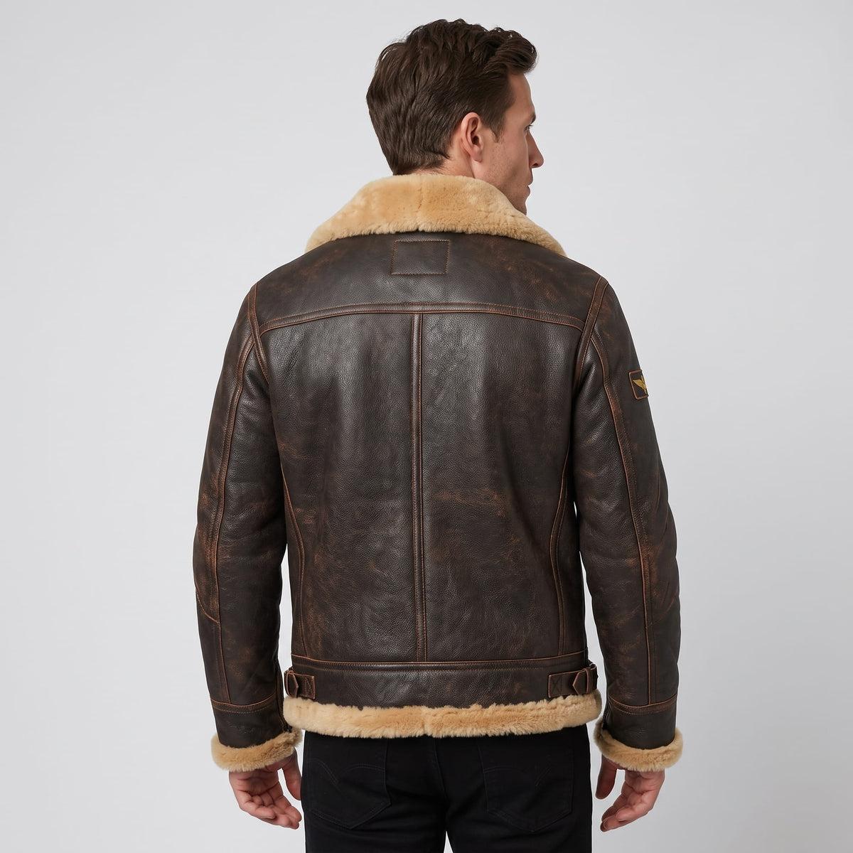 A man wearing a dark brown leather shearling bomber jacket with a sherpa collar, shown from the back