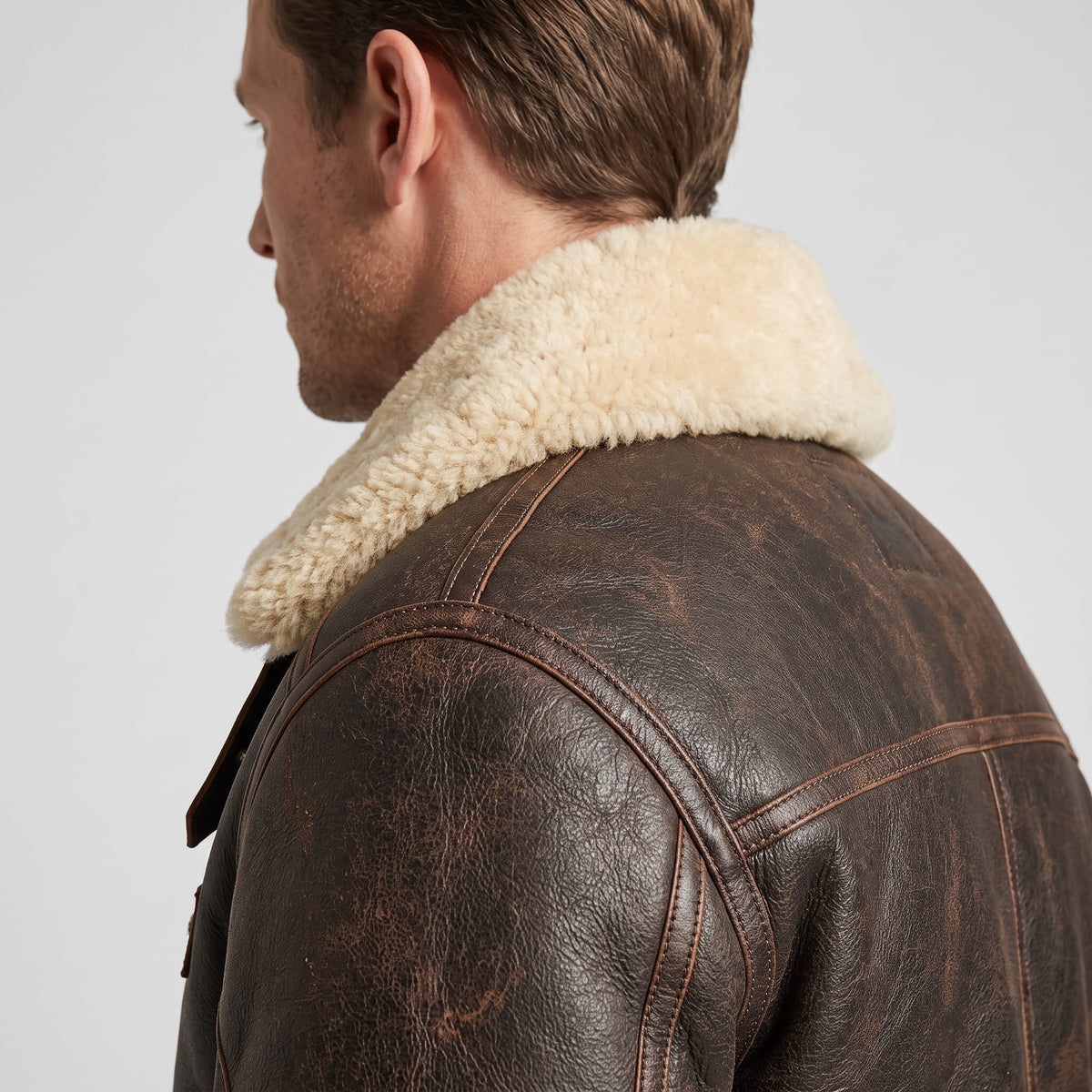 Side view of a man wearing a dark brown leather shearling bomber jacket with a sherpa collar