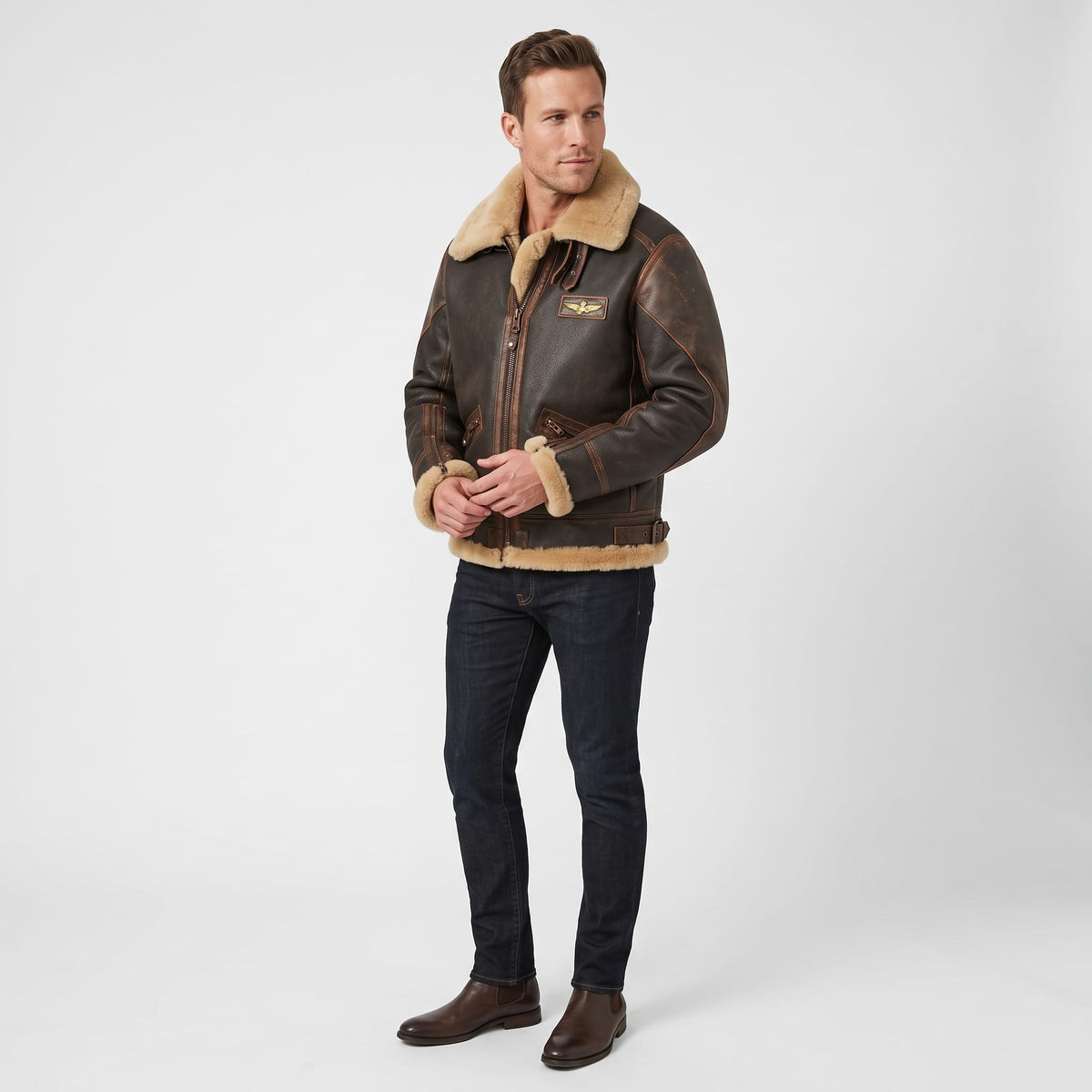 A man wearing a dark brown leather shearling bomber jacket with a sherpa collar and zip pockets, full-length view