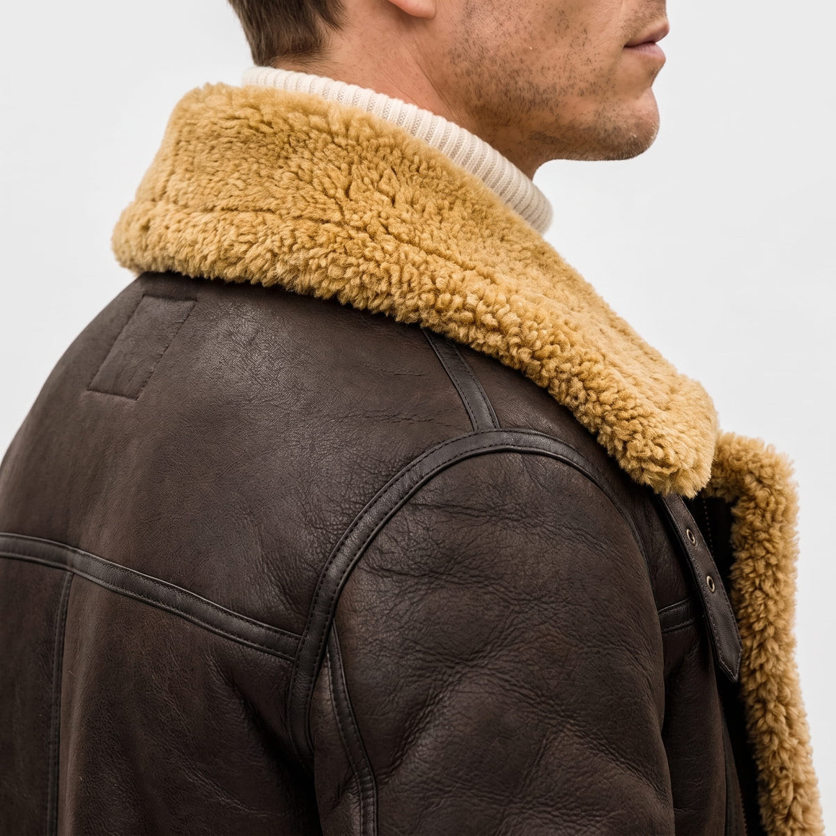 A man wearing a dark brown leather shearling bomber jacket with a sherpa collar, shown from the back