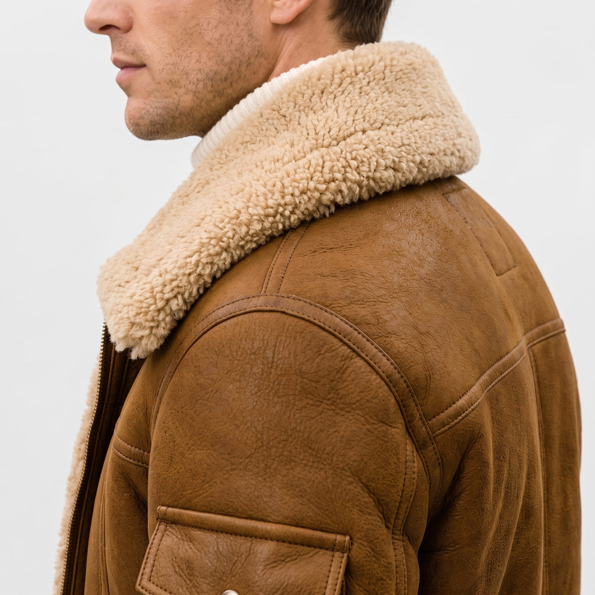 Close-up of a brown leather shearling bomber jacket showing the plush sherpa collar and shoulder detail