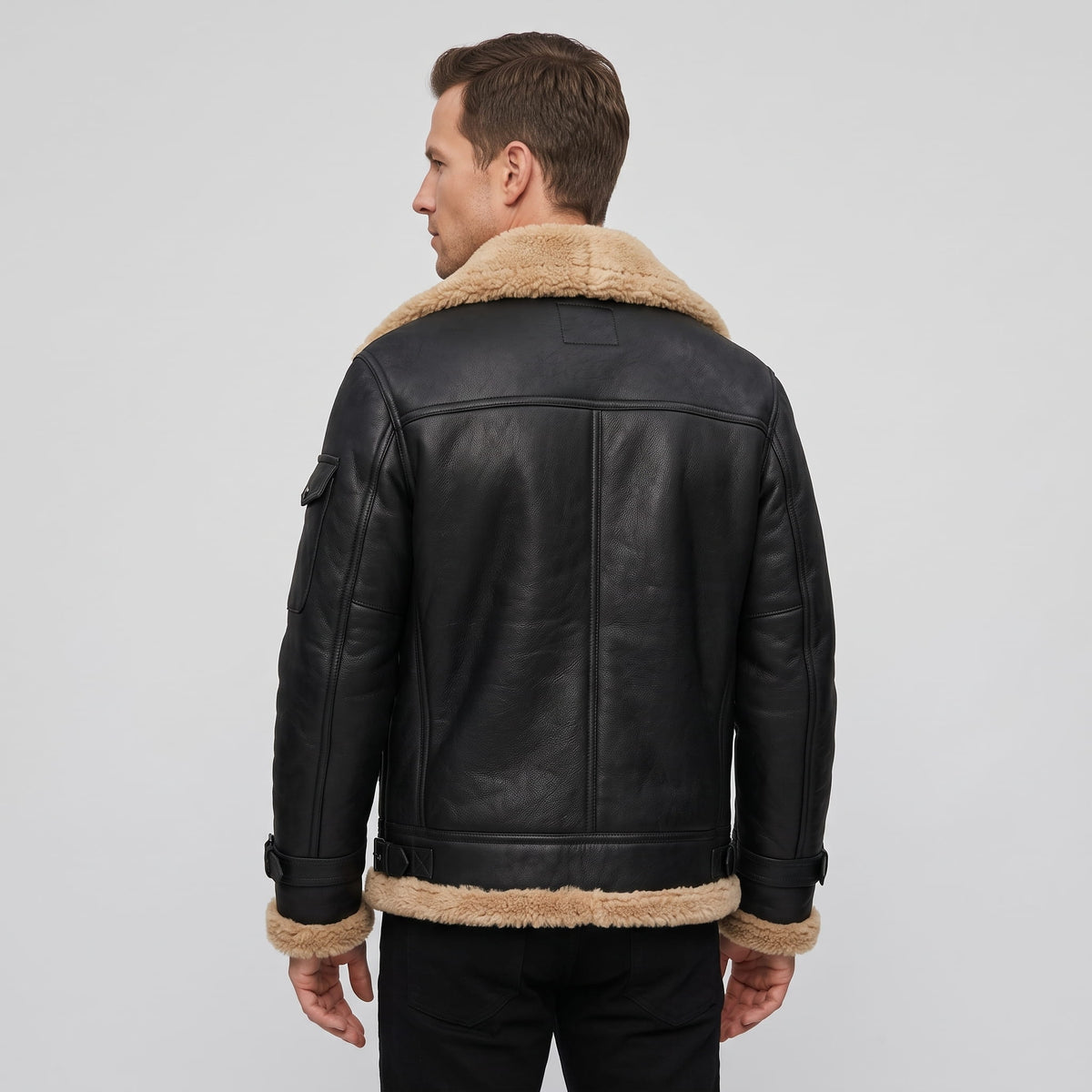 A man wearing a black leather shearling bomber jacket with a sherpa collar, shown from the back