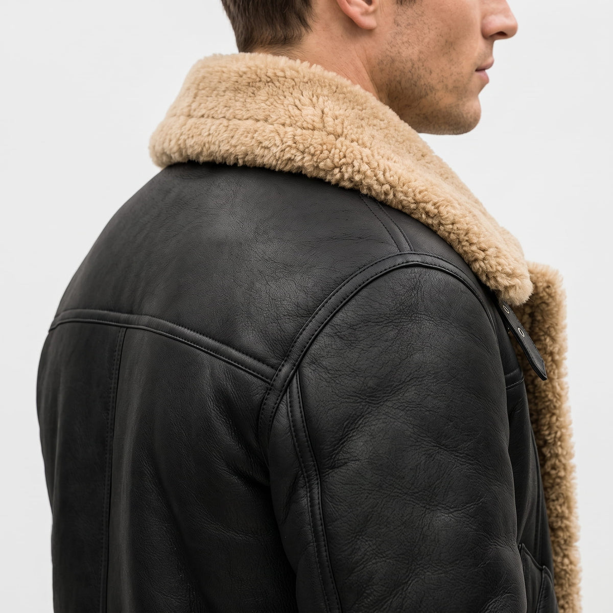Close-up of a black leather shearling bomber jacket showing the plush sherpa collar and back detail