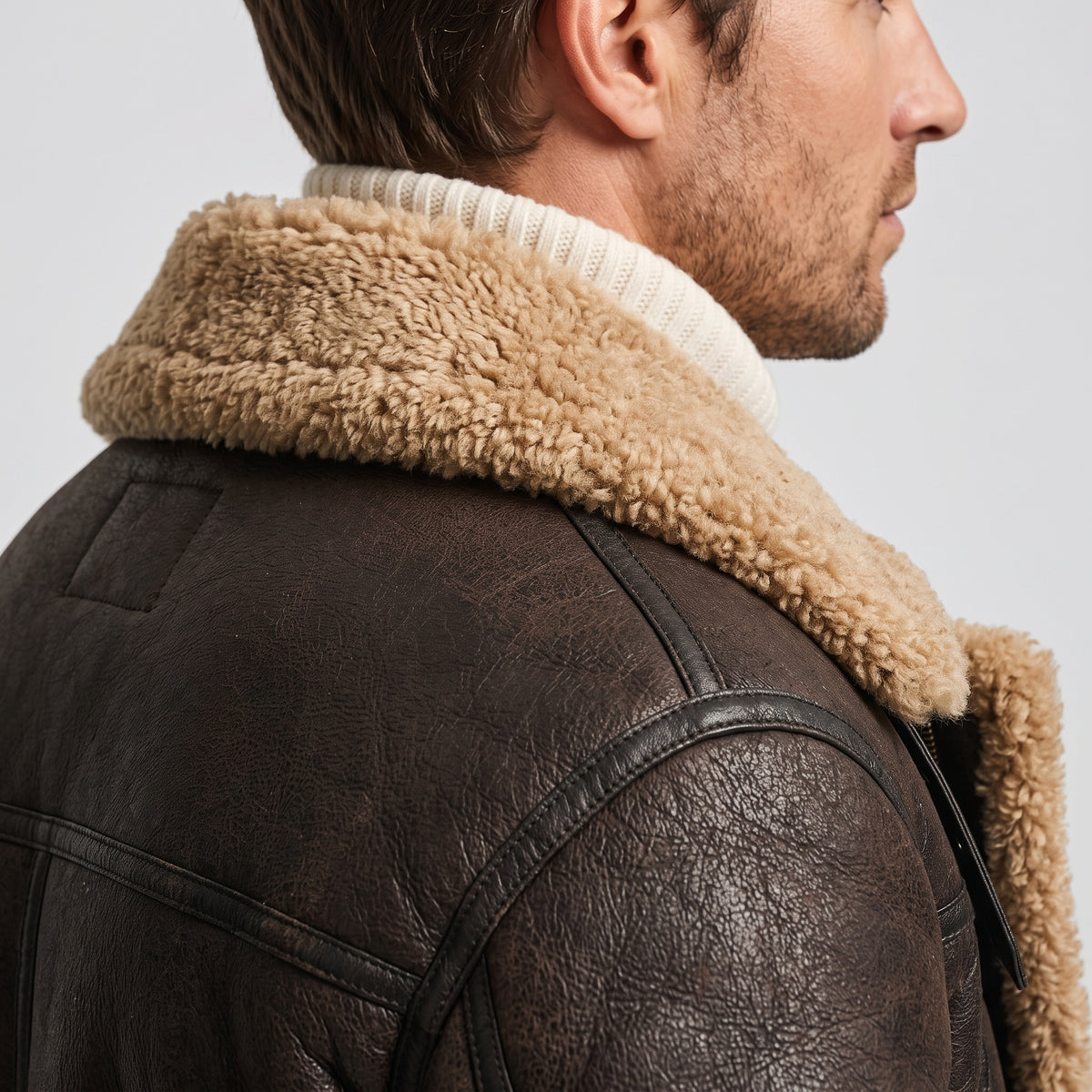 Close-up of a man wearing a black leather shearling jacket, showing the plush fur collar and leather texture