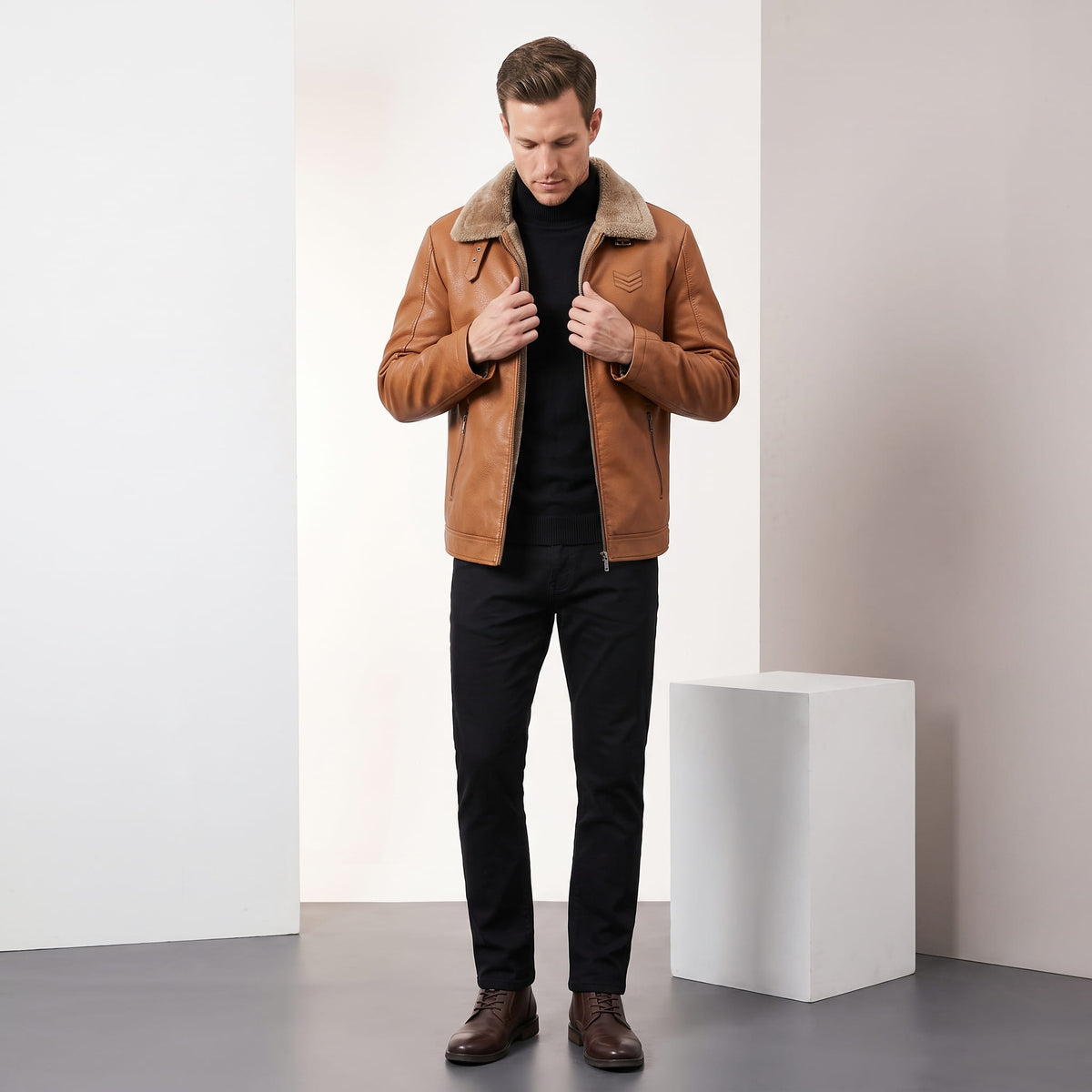 A man wearing a brown leather shearling jacket with a plush collar and full-zip front, standing indoors