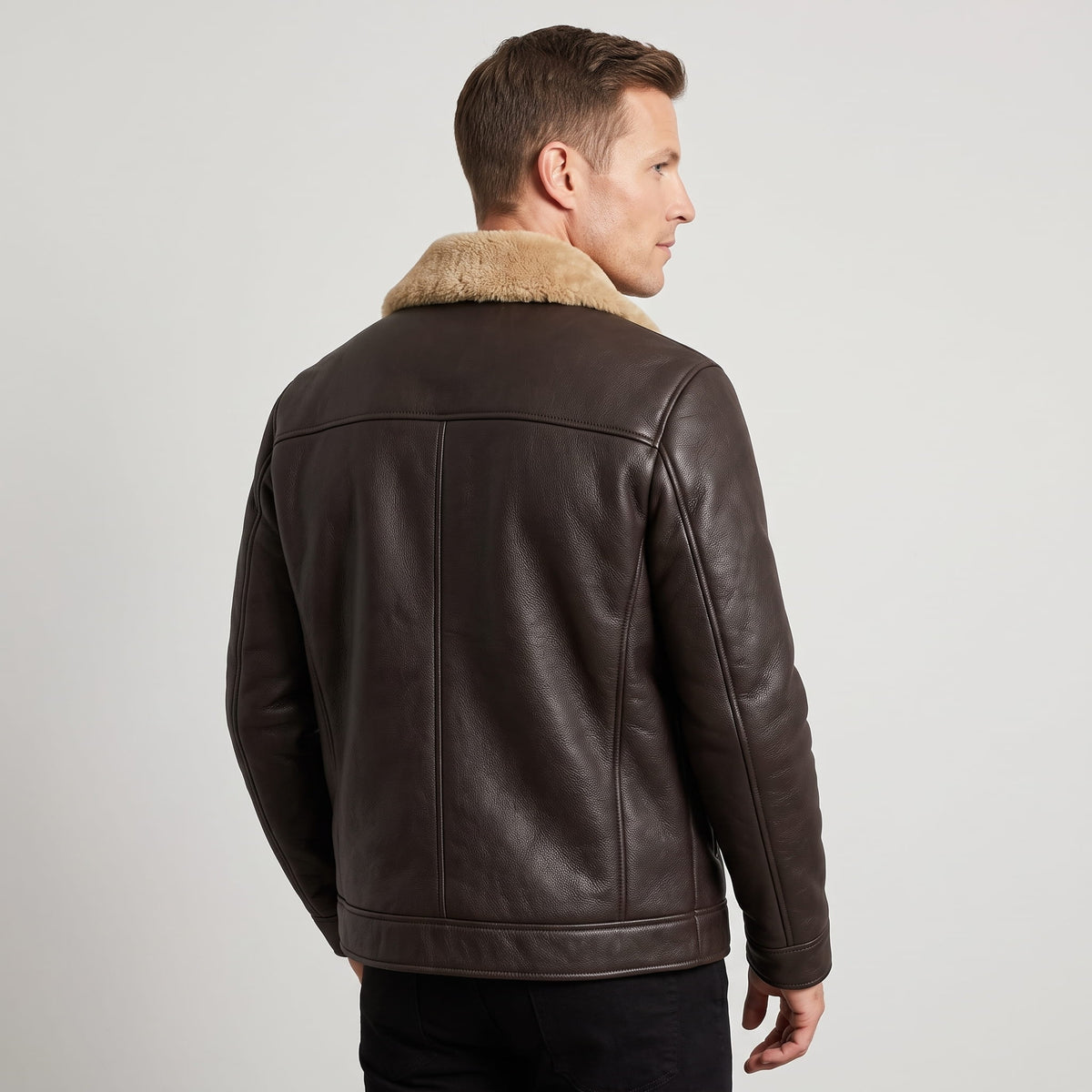 A man wearing a dark brown leather shearling jacket with a plush collar, shown from the back