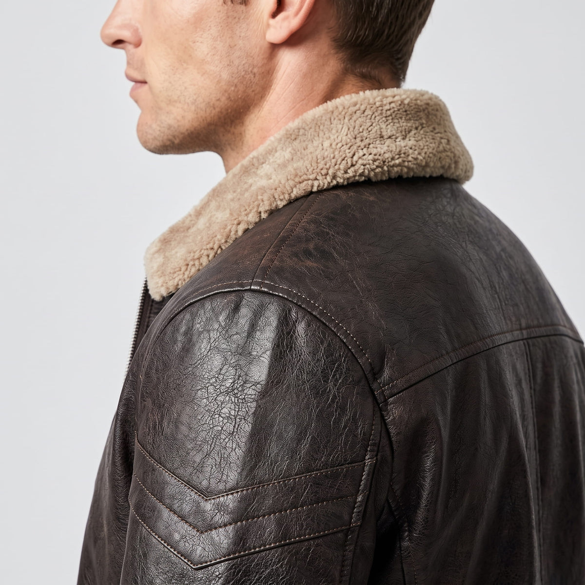 Close-up side view of a dark brown leather shearling jacket showing the plush collar and shoulder detail