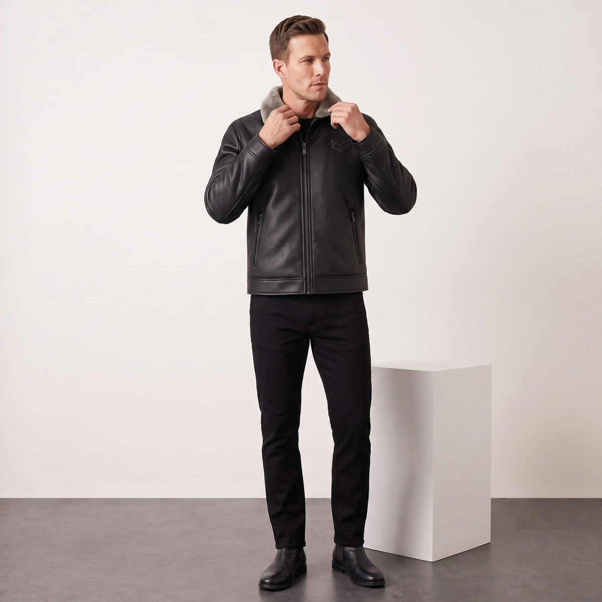 A man wearing a black leather shearling jacket with a plush collar and full-zip front, full-length view