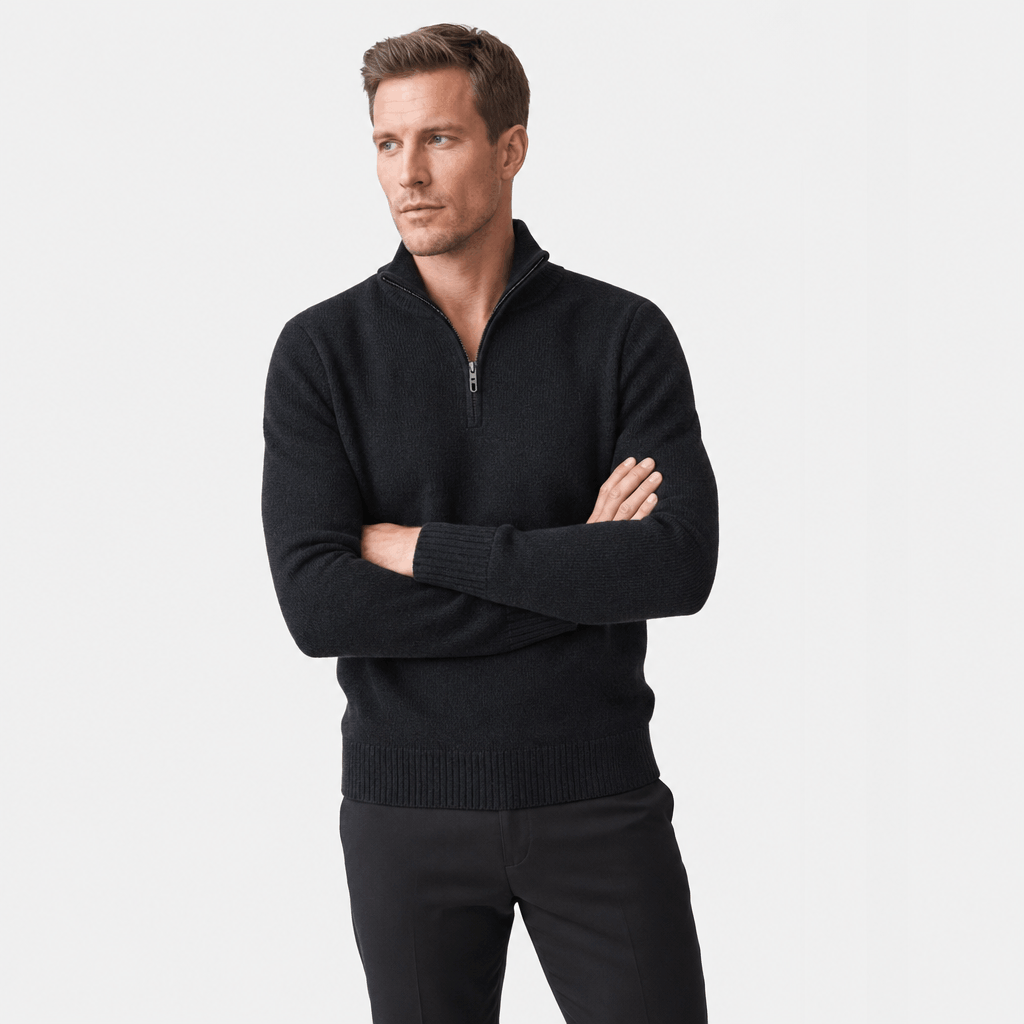 Man wearing a black textured half-zip sweater with black pants, shown standing with his arms crossed.