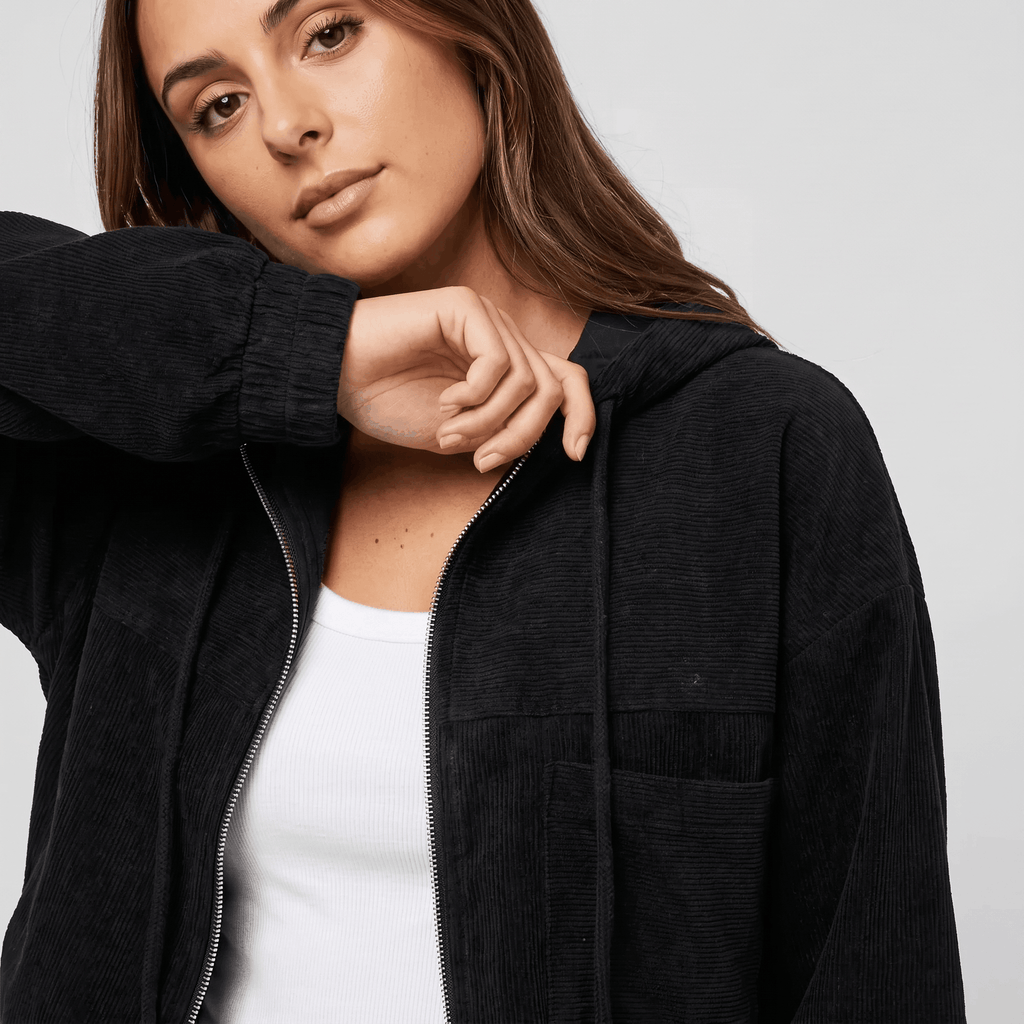 Black corduroy zip-up hoodie with a textured ribbed surface, drawstring hood, and relaxed fit over a white base layer.