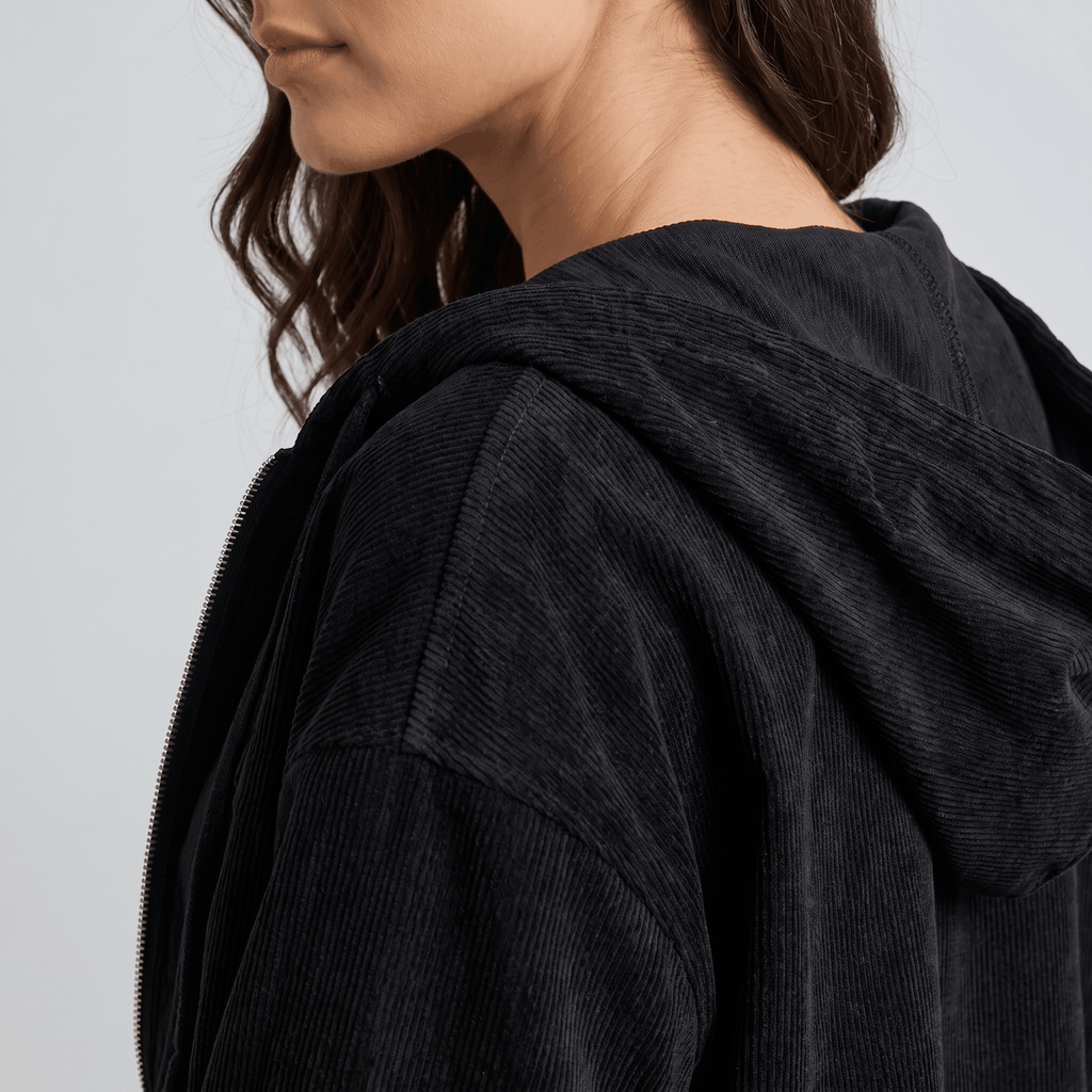 Black corduroy zip-up hoodie with a textured wale surface, drawstring hood, and relaxed layering fit.