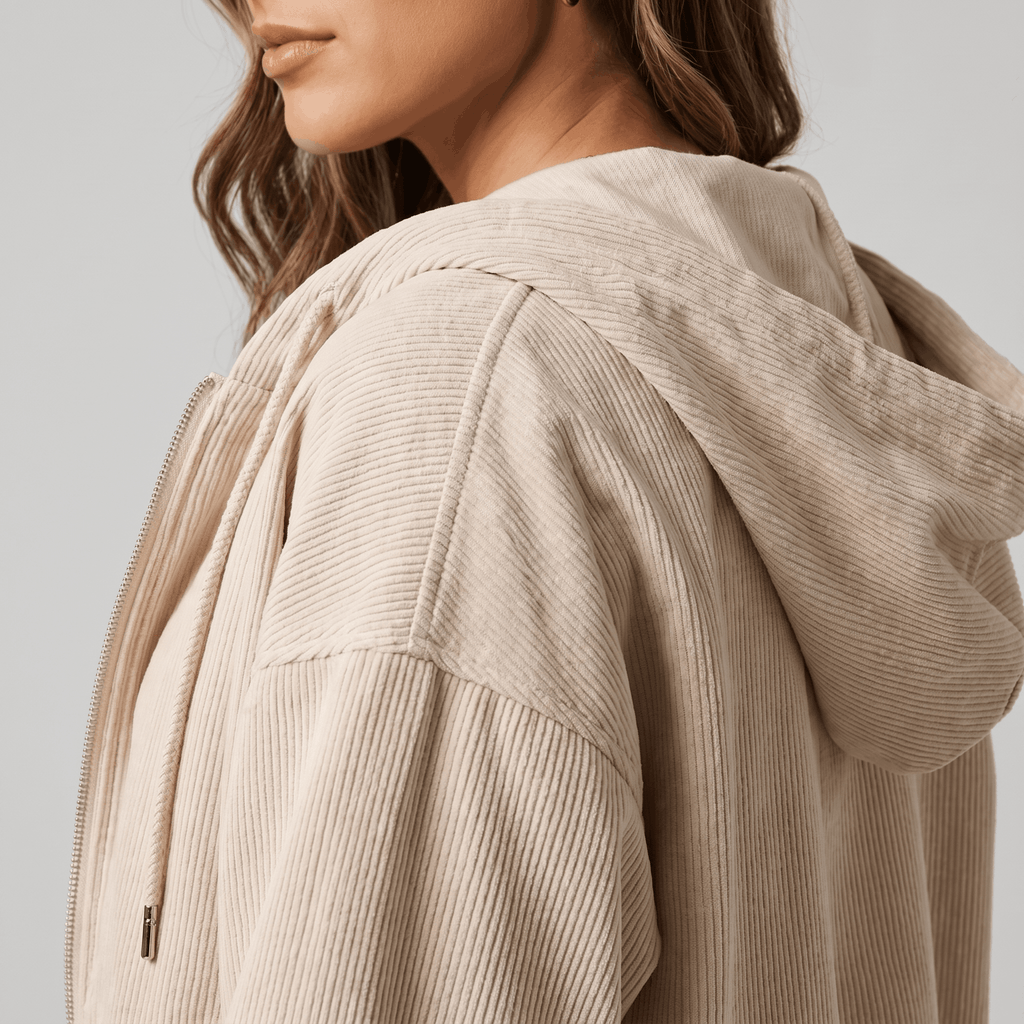 Beige corduroy zip-up hoodie with a soft wale texture, drawstring hood, and relaxed, oversized fit.