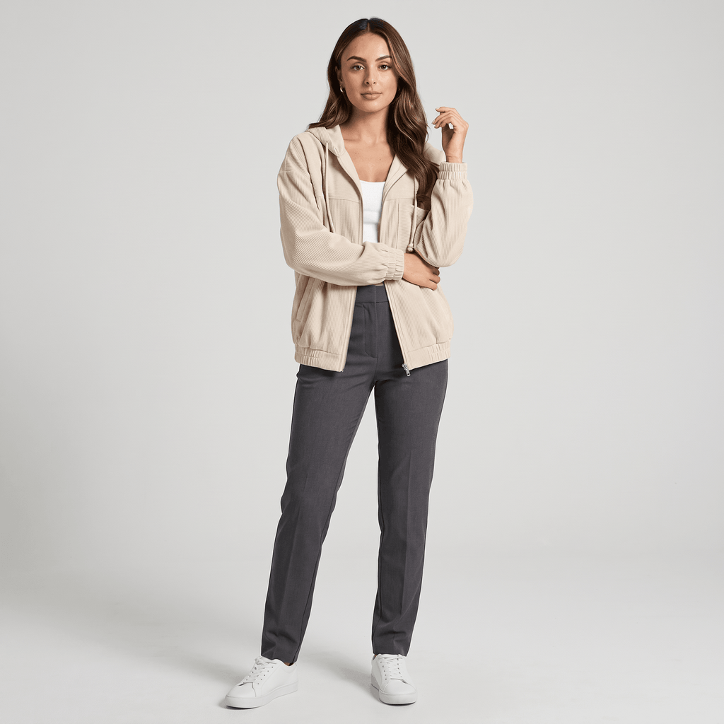 Beige corduroy zip-up hoodie with a drawstring hood and elasticated cuffs, worn over a white top and grey trousers.