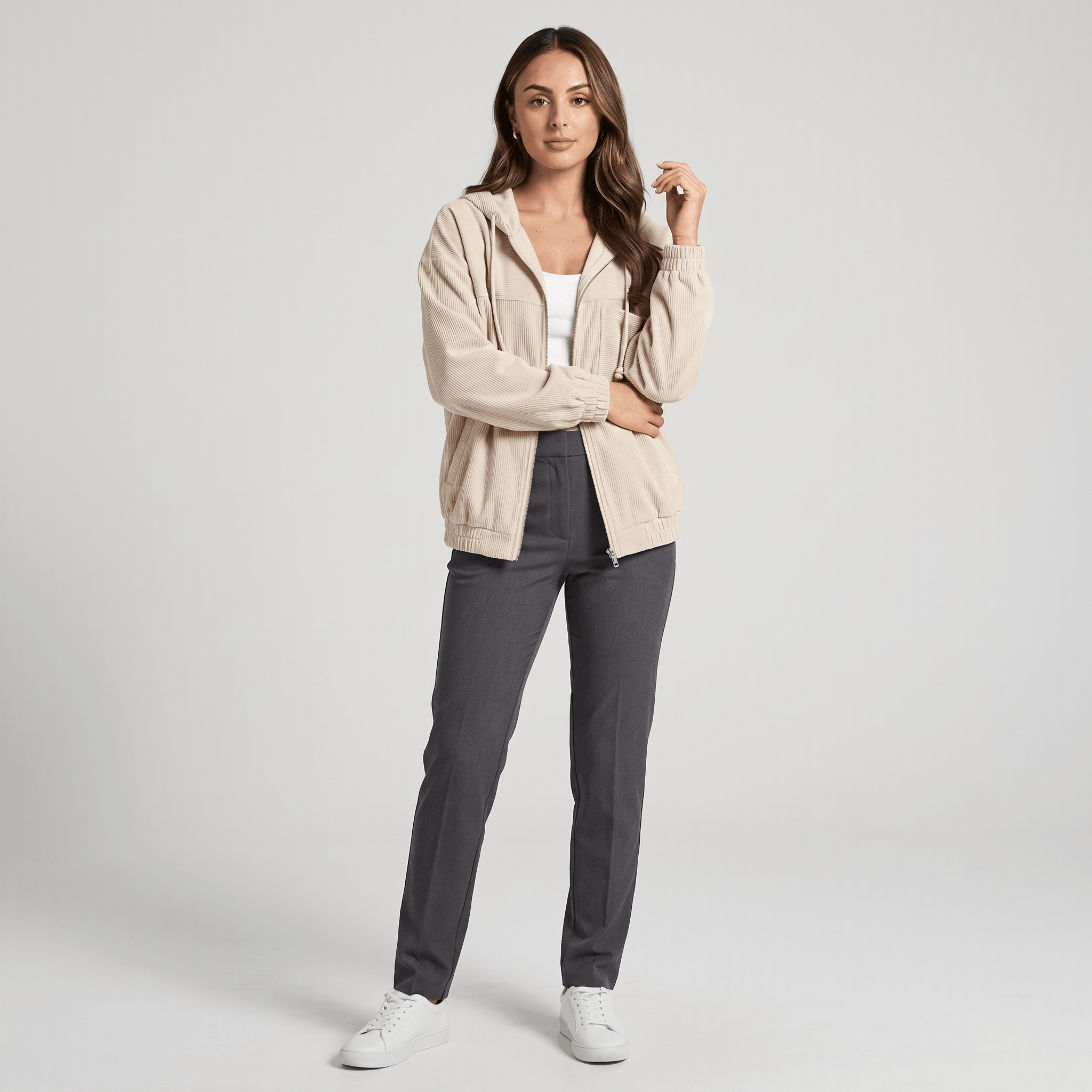 Beige corduroy zip-up hoodie with a drawstring hood and elasticated cuffs, worn over a white top and grey trousers.