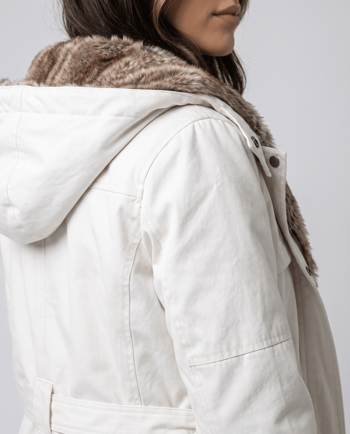 Close-up of a woman wearing a white long parka coat, showing the fur-lined hood and adjustable waist detail