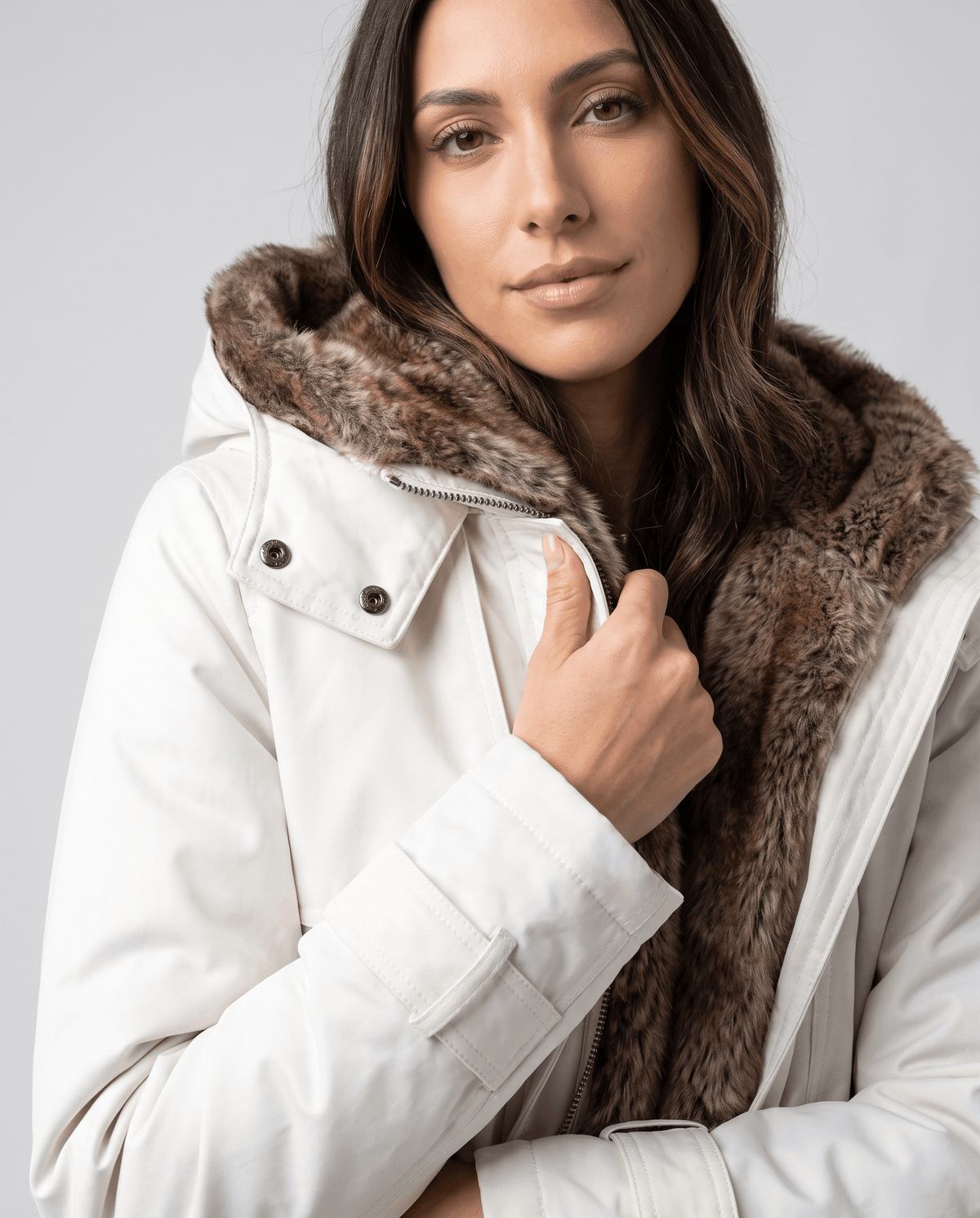 Close-up of a woman wearing a white long parka coat with a fur-lined hood and adjustable waist
