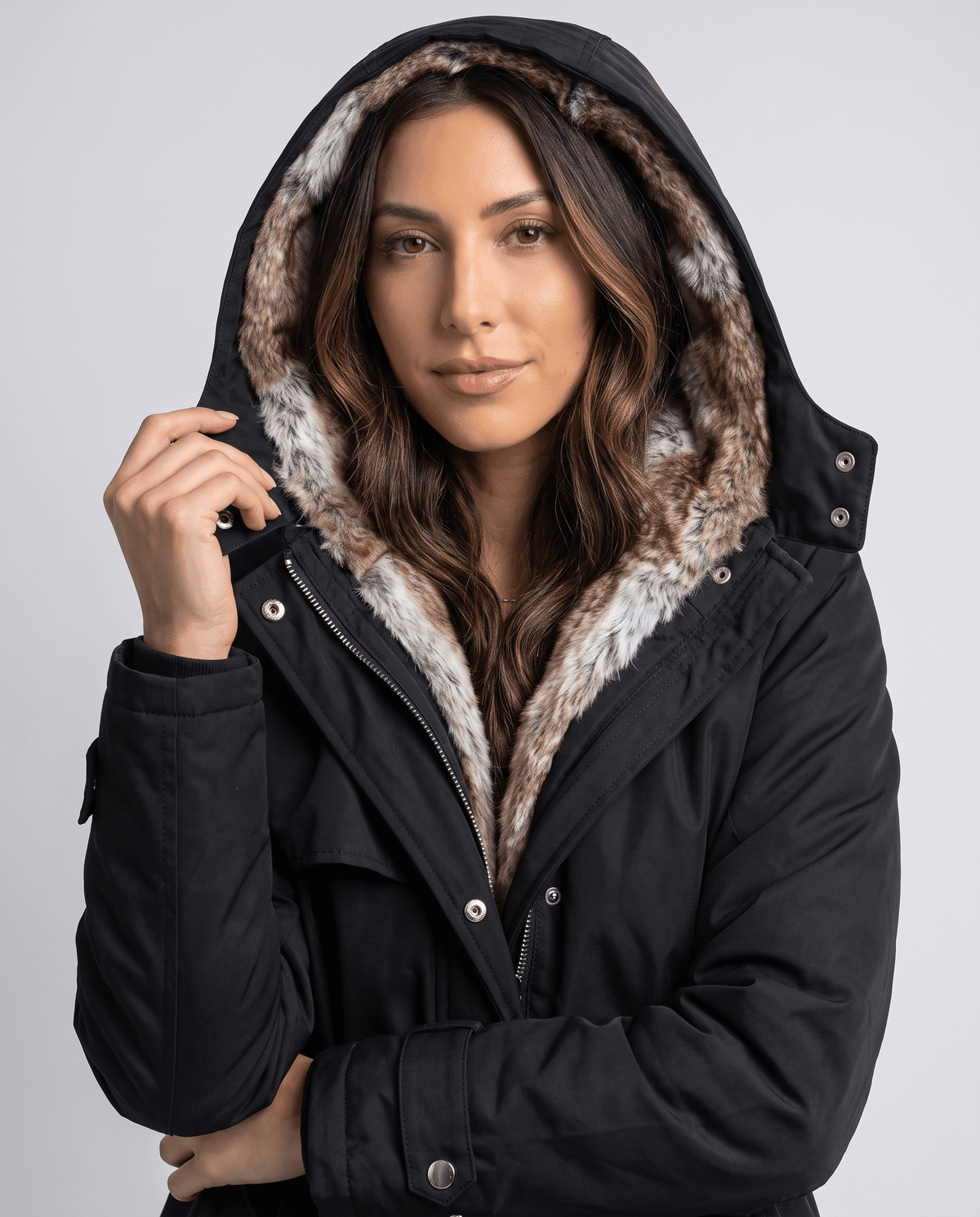 A woman wearing a black long parka coat with a fur-lined hood, shown adjusting the hood