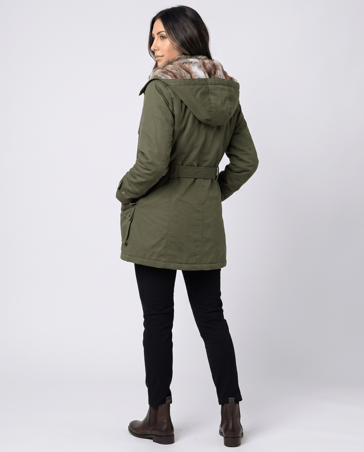 A woman wearing an olive green long parka coat with fur lining, a hood, and an adjustable waist, back view