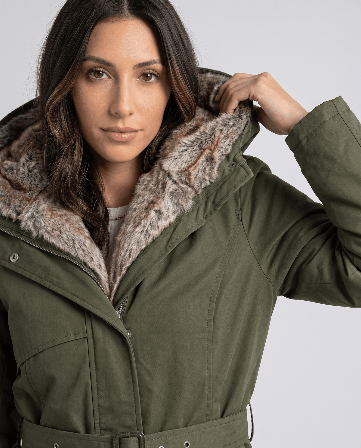 Close-up of a woman wearing an olive green parka coat, showing the fur-lined hood and adjustable waist