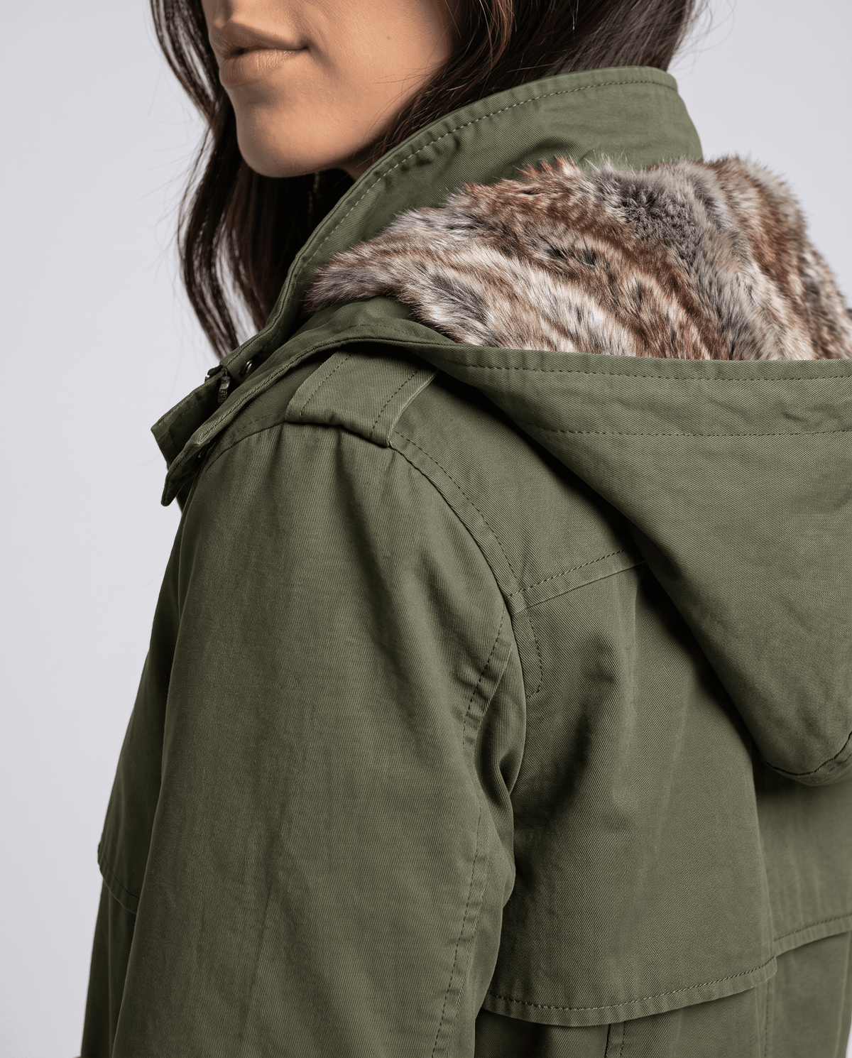 Close-up of a woman wearing an olive green parka coat, showing the fur-lined hood and shoulder detail