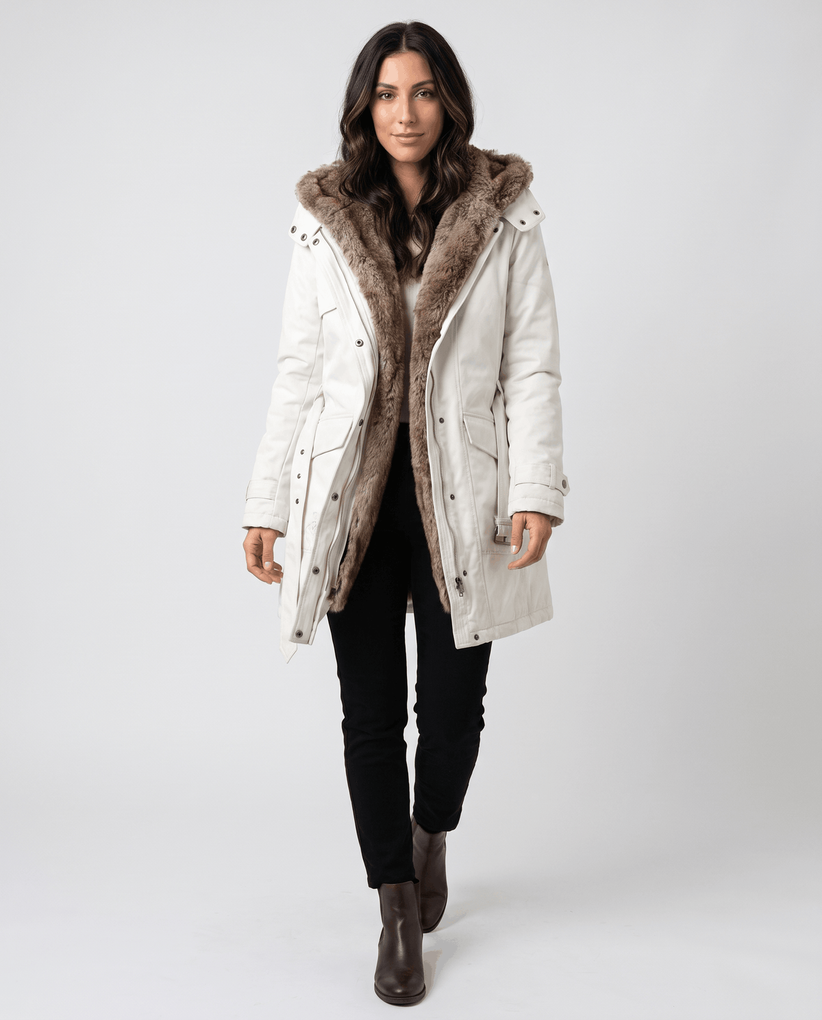 A woman wearing a white long parka coat with fur lining, a hood, and an adjustable waist, full-body view