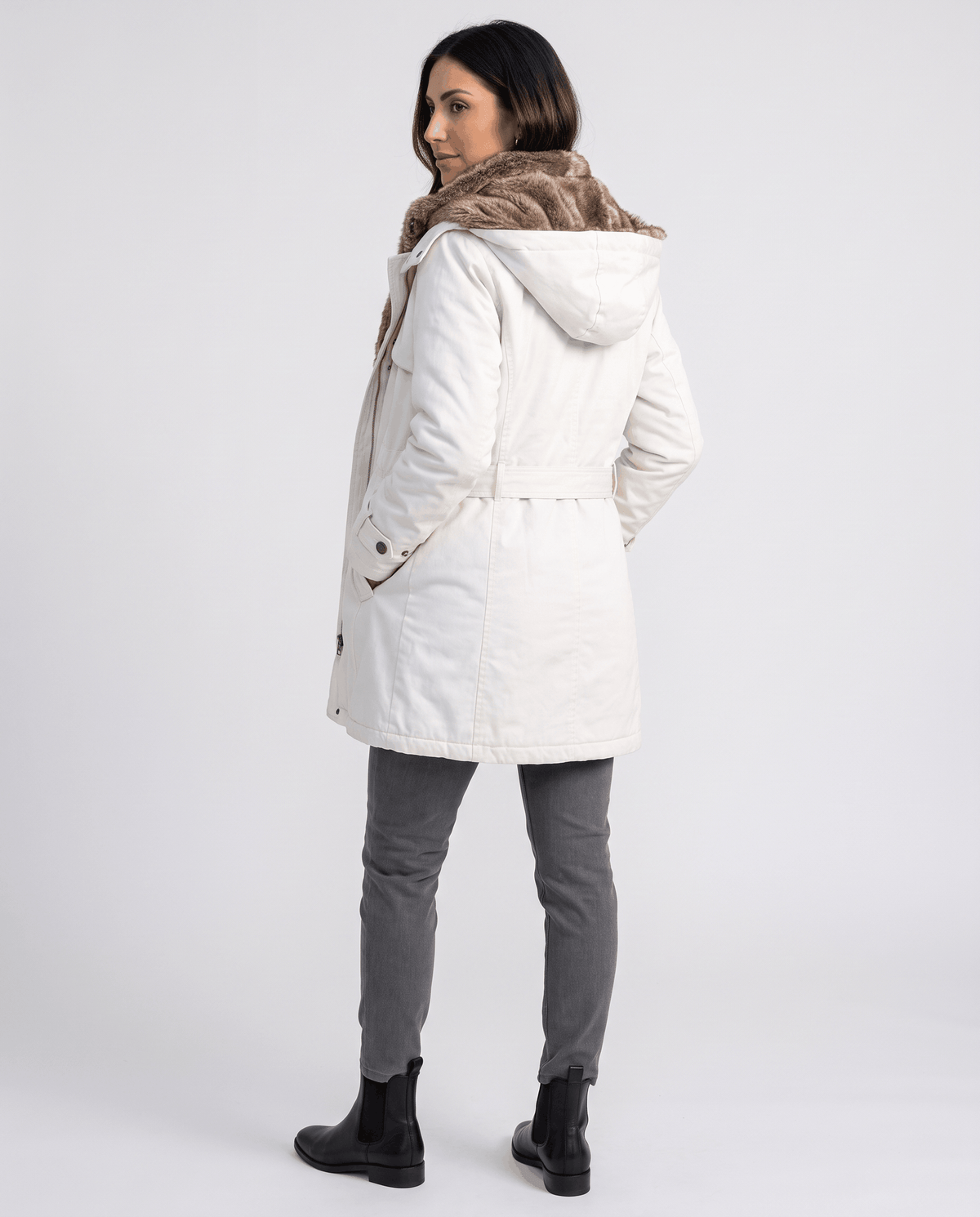 A woman wearing a white long parka coat with fur lining, a hood, and an adjustable waist, back view