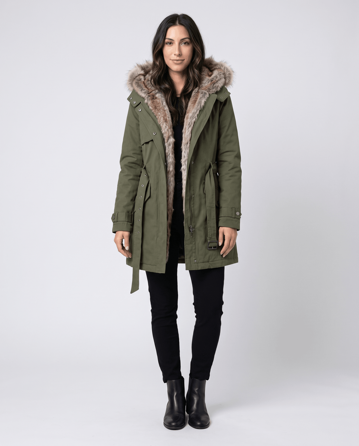A woman wearing a long olive green parka coat with fur lining, a hood, and an adjustable waist